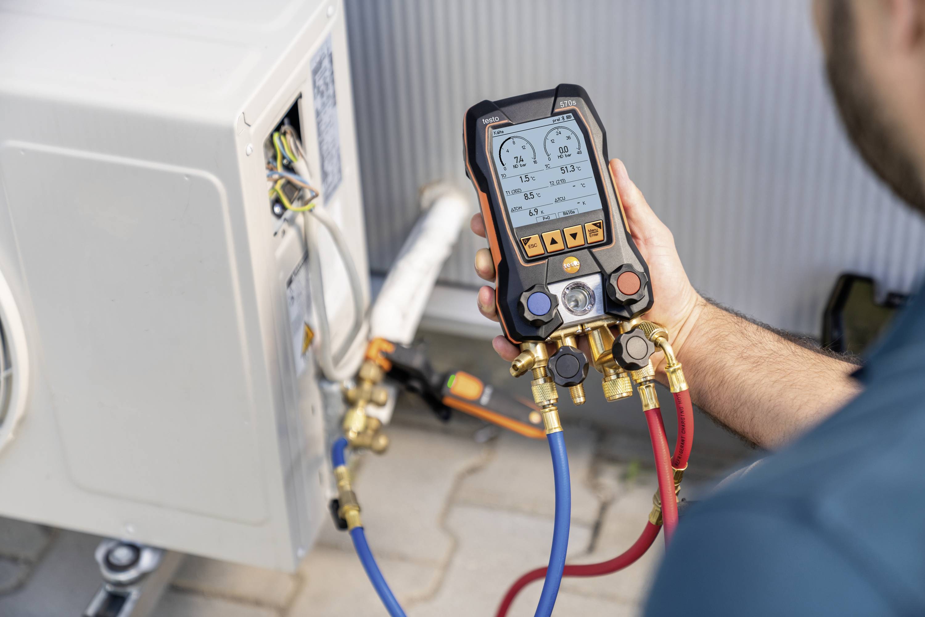 A person is inspecting an air conditioning unit with a digital manometer to measure pressure values. Calibrated tool and cable are visible.