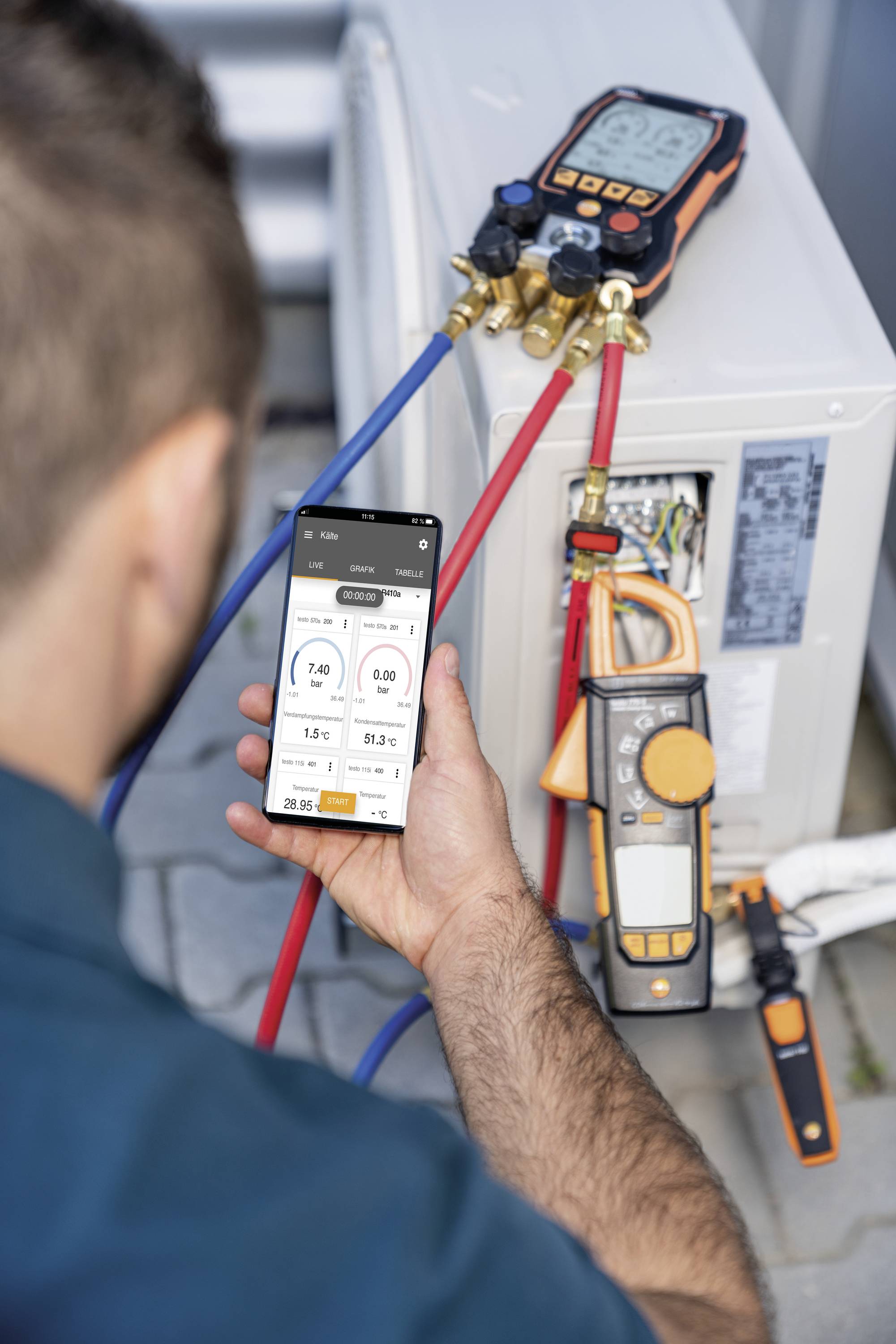 A man is checking the settings of an air conditioning unit using a smartphone and instruments. Temperature and pressure are being measured.