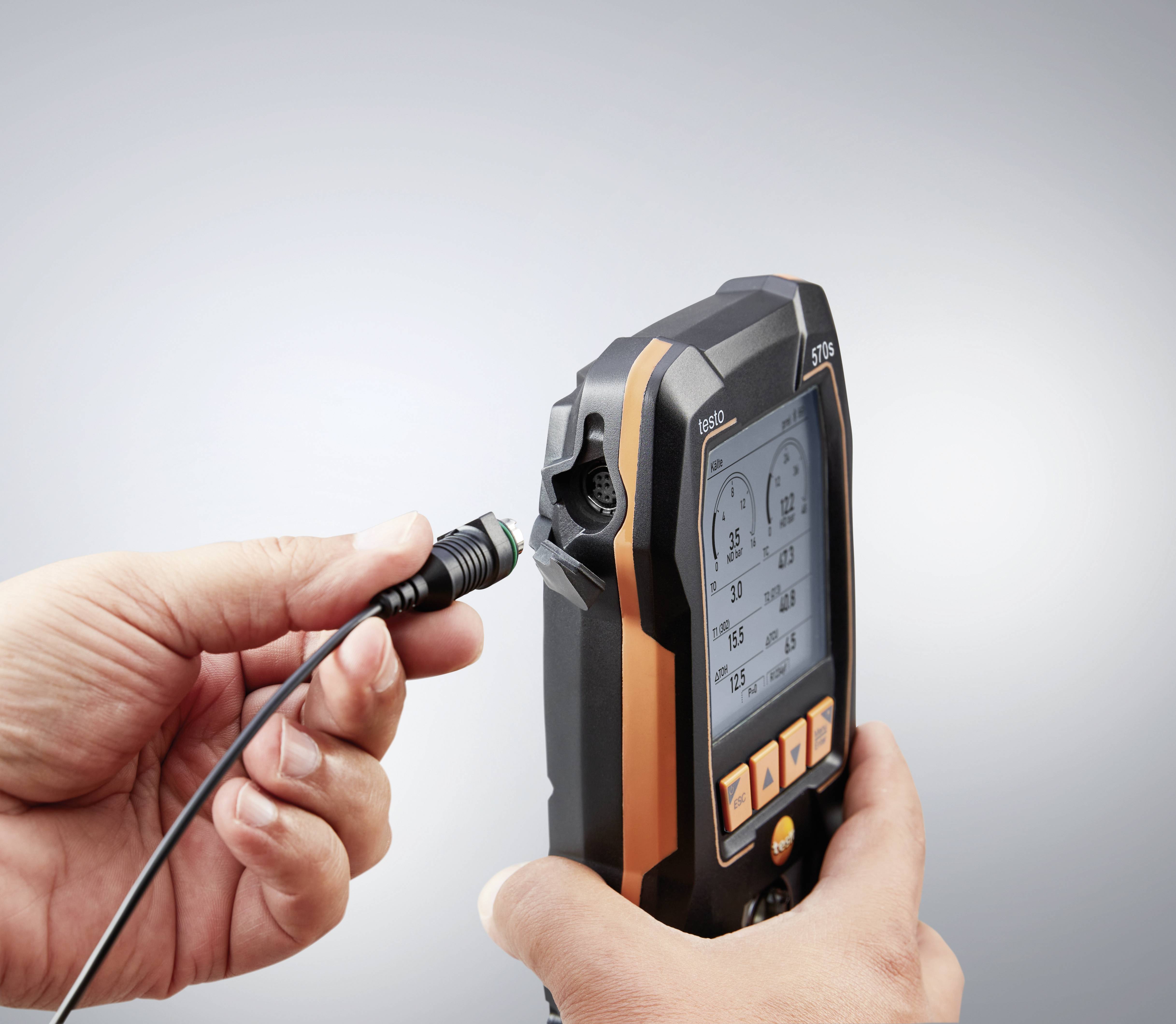A person is holding a portable analysis device that is to be connected via a cable. The display shows data for monitoring systems.