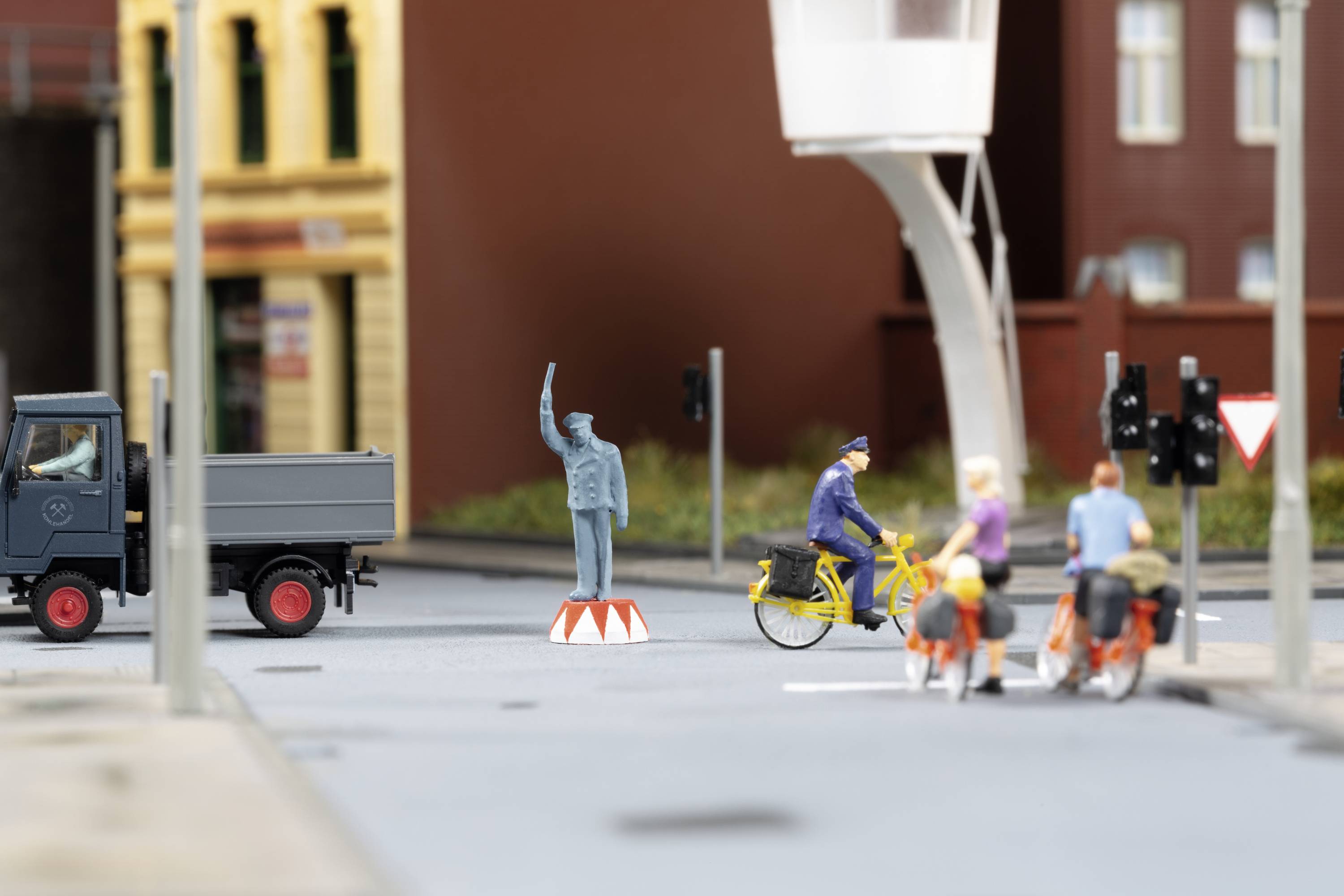 A miniature scene with a lorry, a cyclist, a traffic policeman and a statue in an urban environment.
