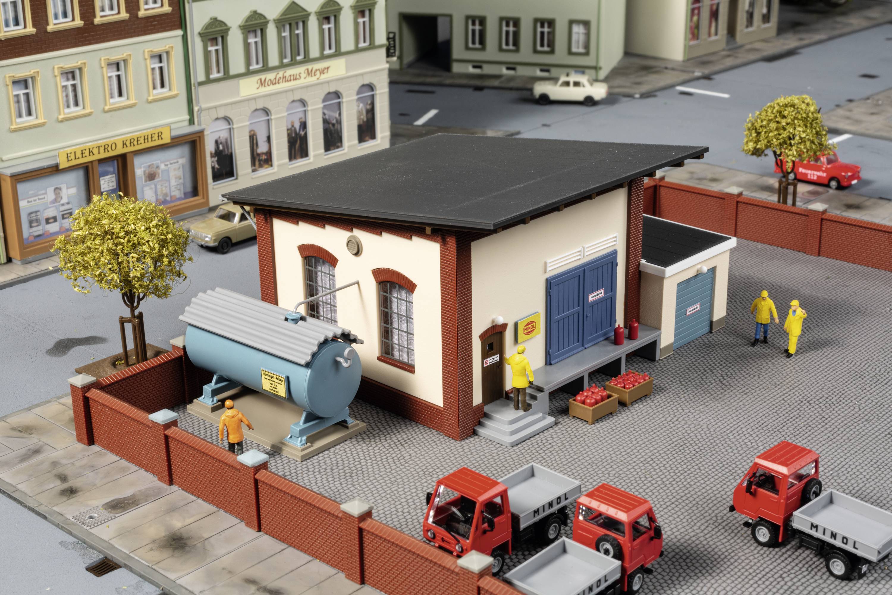 A miniature model of an urban environment with buildings, lorries, figures and trees. One scene depicts deliveries.