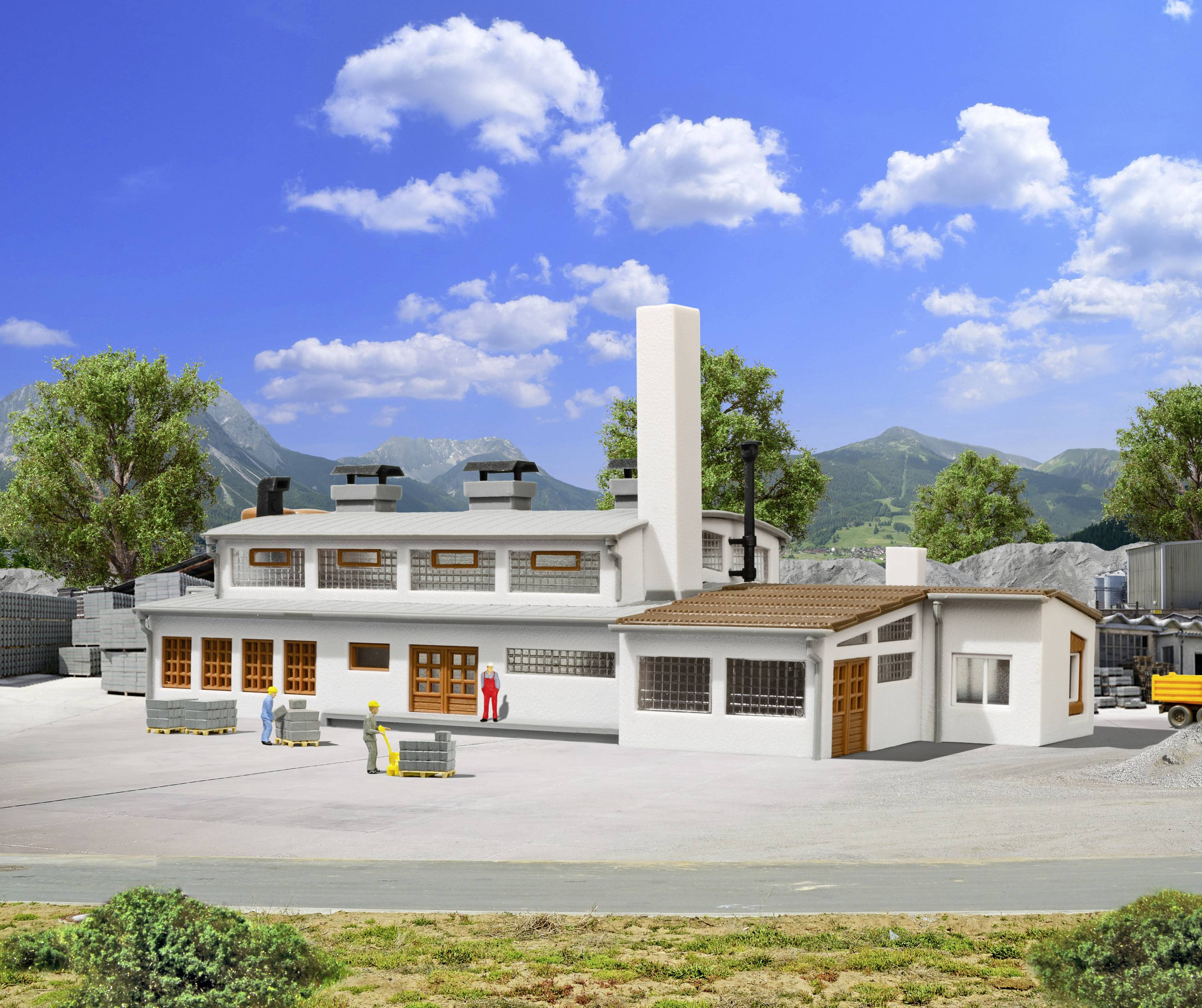 A small industrial premises in a rural setting, surrounded by mountains and trees. Workers are standing in front of the building.
