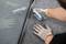 A person is cutting grey carpet flooring with a carpet knife near a glass edge. Hands are wearing work gloves.