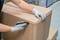 A person wearing grey gloves carefully opens a large cardboard box with a black utility knife in a warehouse environment.