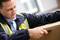A man in work attire opens a cardboard box with a utility knife. He is wearing a high-visibility safety vest and appears focused on his task.
