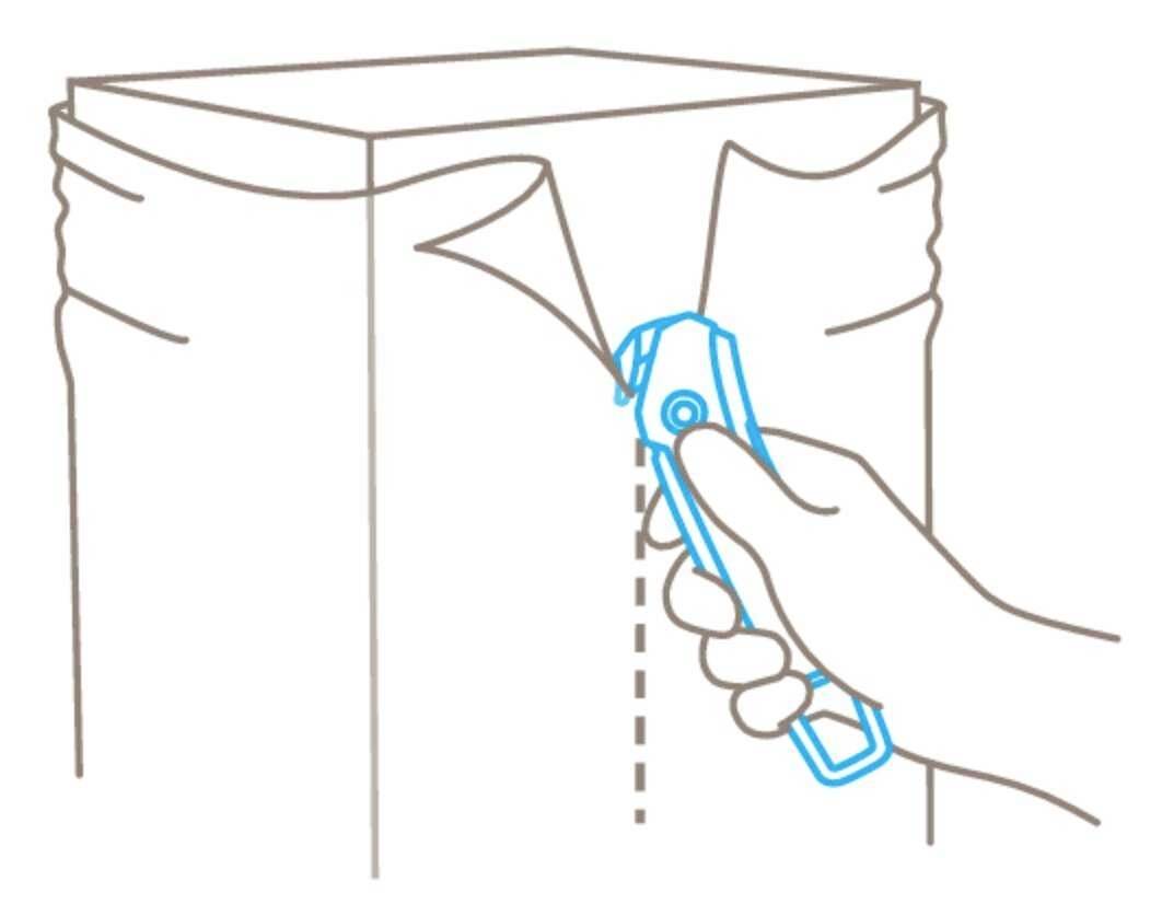A hand opens a bag using a cutting tool along the marked line.