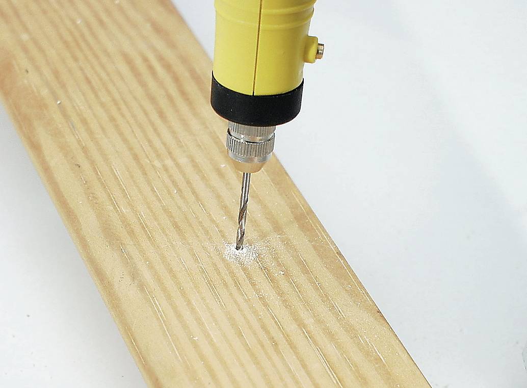 A yellow drill is boring a hole into a light-coloured wooden board. Wood shavings are gathering around the drilling point.
