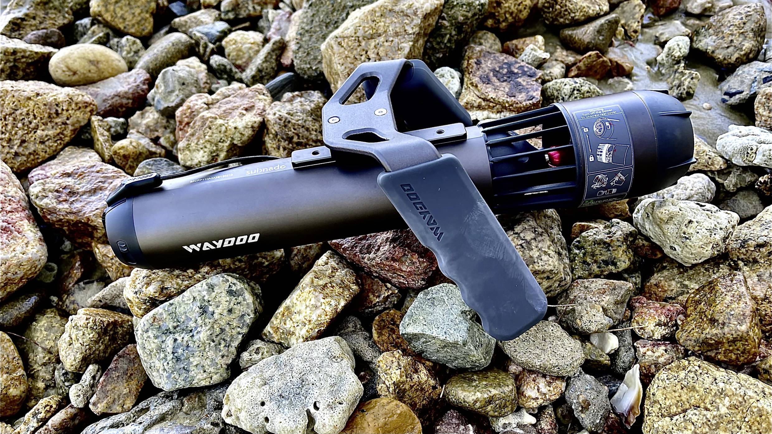 A black water scooter lies on a rocky beach. The name 'Waydoo' is visible on the side. Suitable for water sports activities.