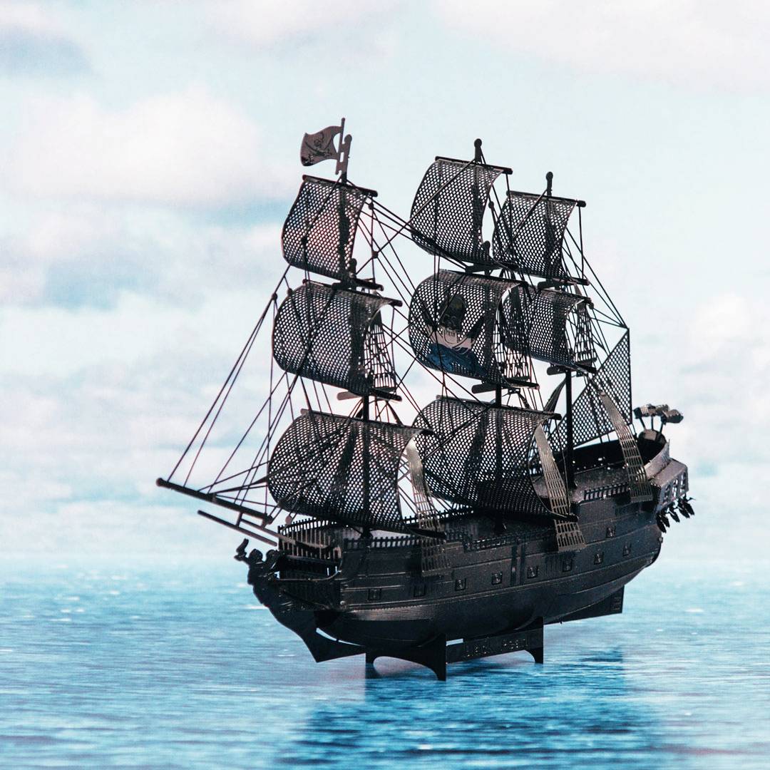 An old sailing ship sails across the sea, fitted with black sails. The sky is cloudy, the sea calm.
