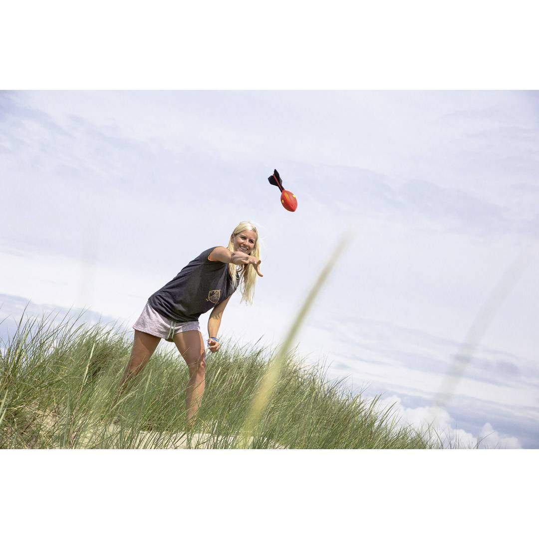 A person throws a dog toy in a grassy dune landscape. The sky is cloudy.