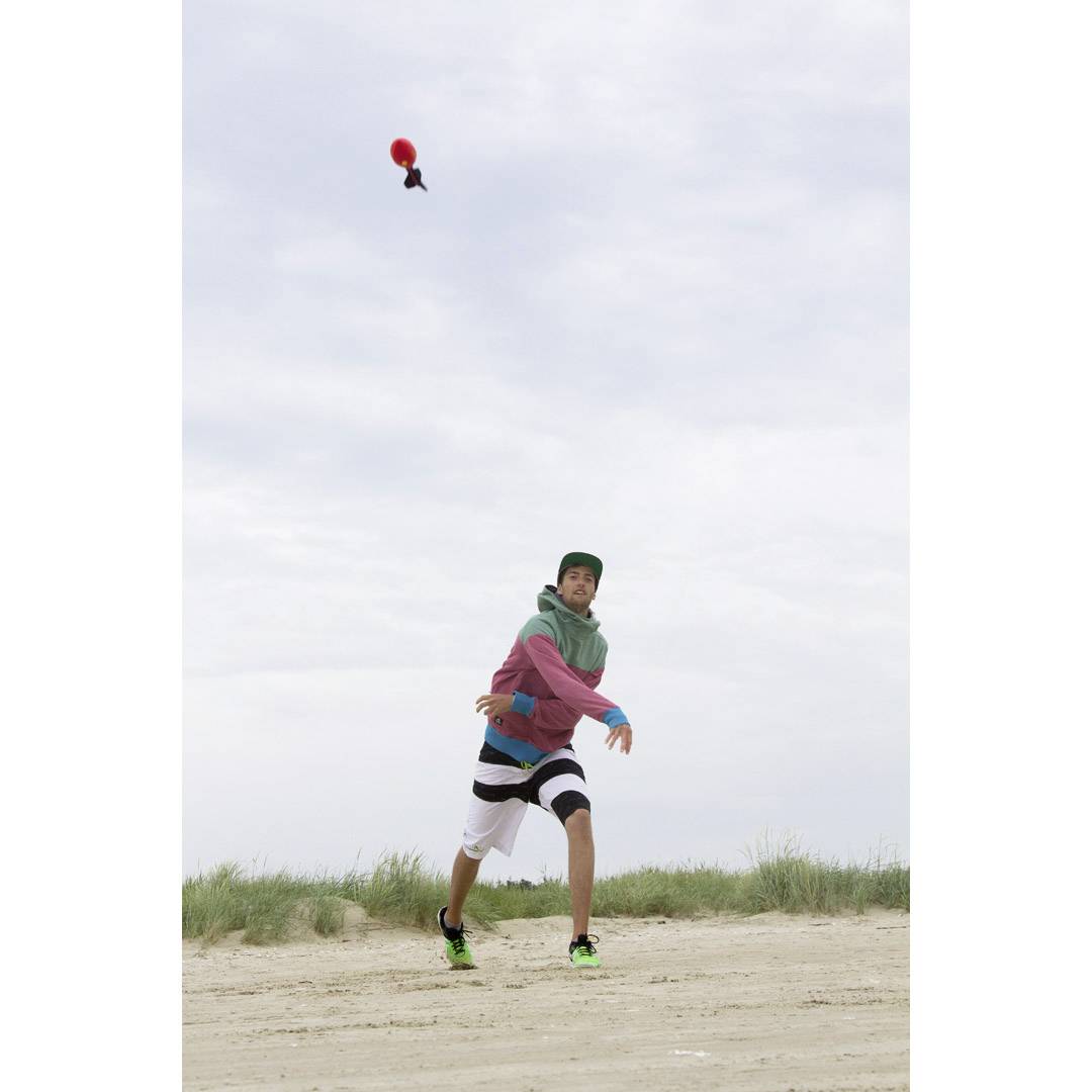 A person on the beach throws a red Poké Ball into the air. A cloudy sky is visible in the background.