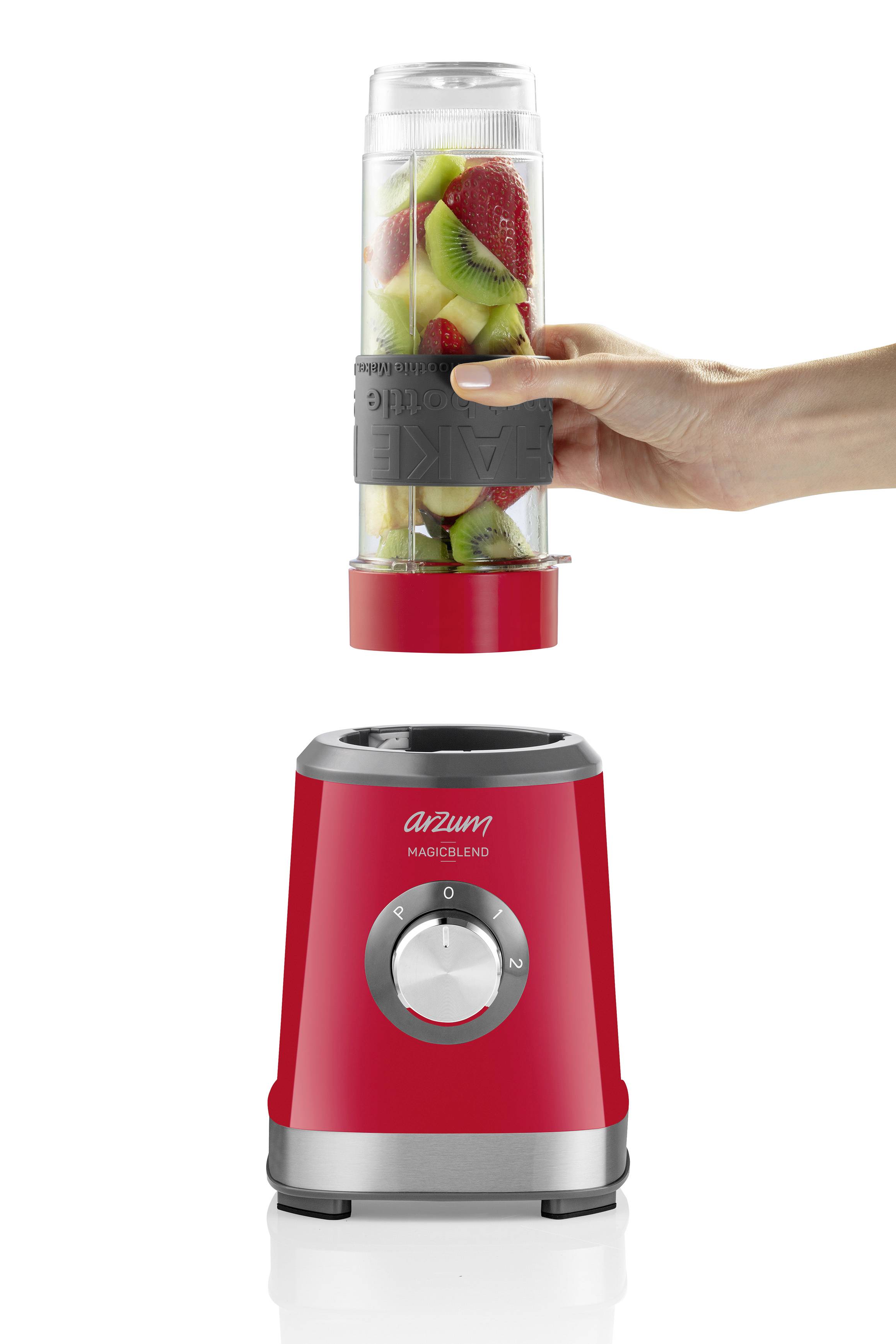 A hand is holding a container filled with fruit over a red blender.