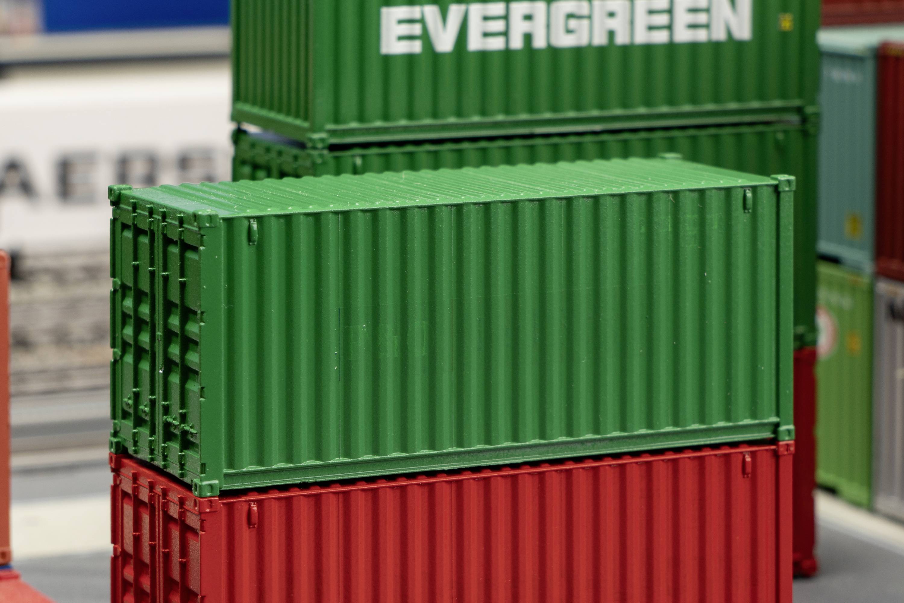 Green and red freight containers stacked in a port warehouse, with the 'Evergreen' lettering on one of the containers in the background.