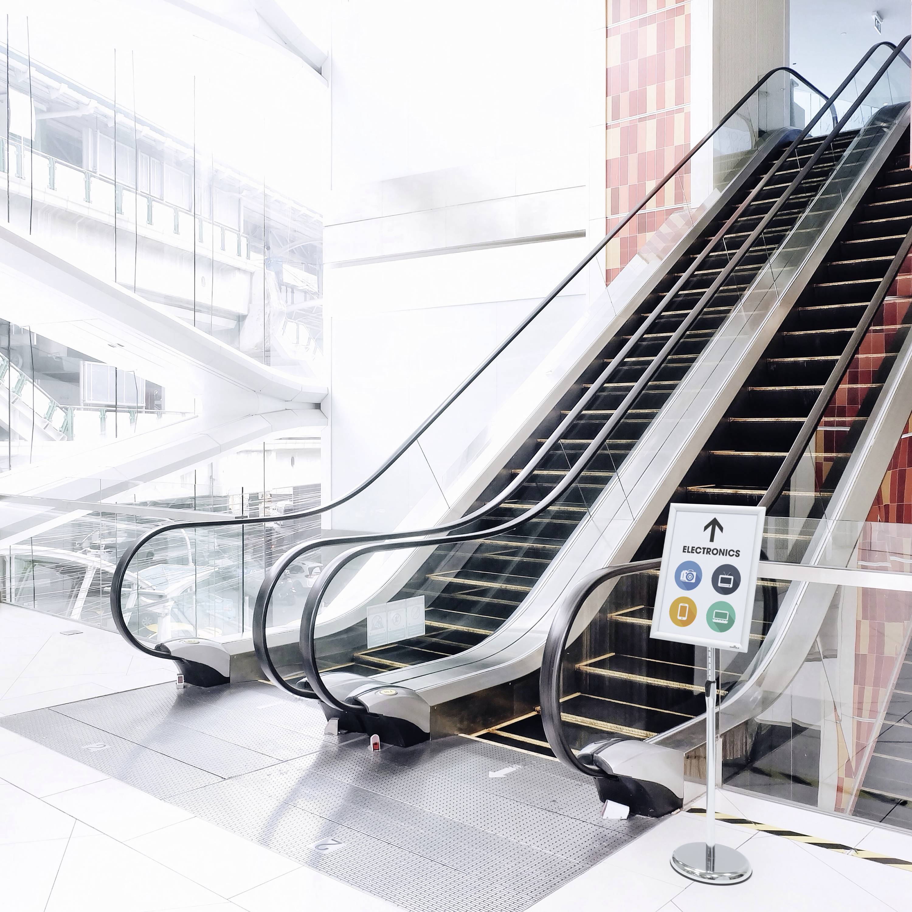 An escalator in a modern, bright shopping centre. A sign indicates that the escalator is out of order.