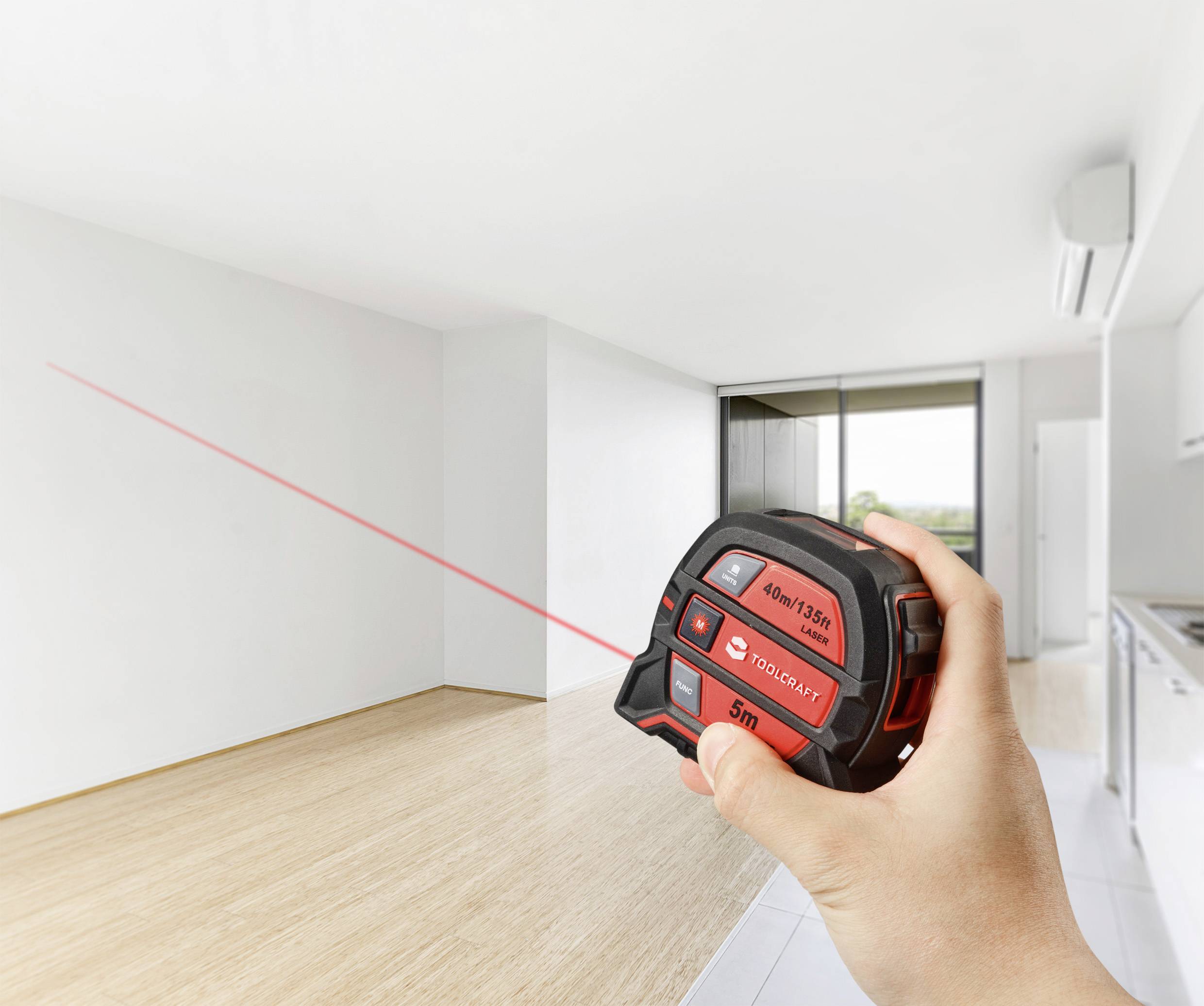 A person is measuring the room of a modern, empty flat with a wooden floor using a laser distance meter.