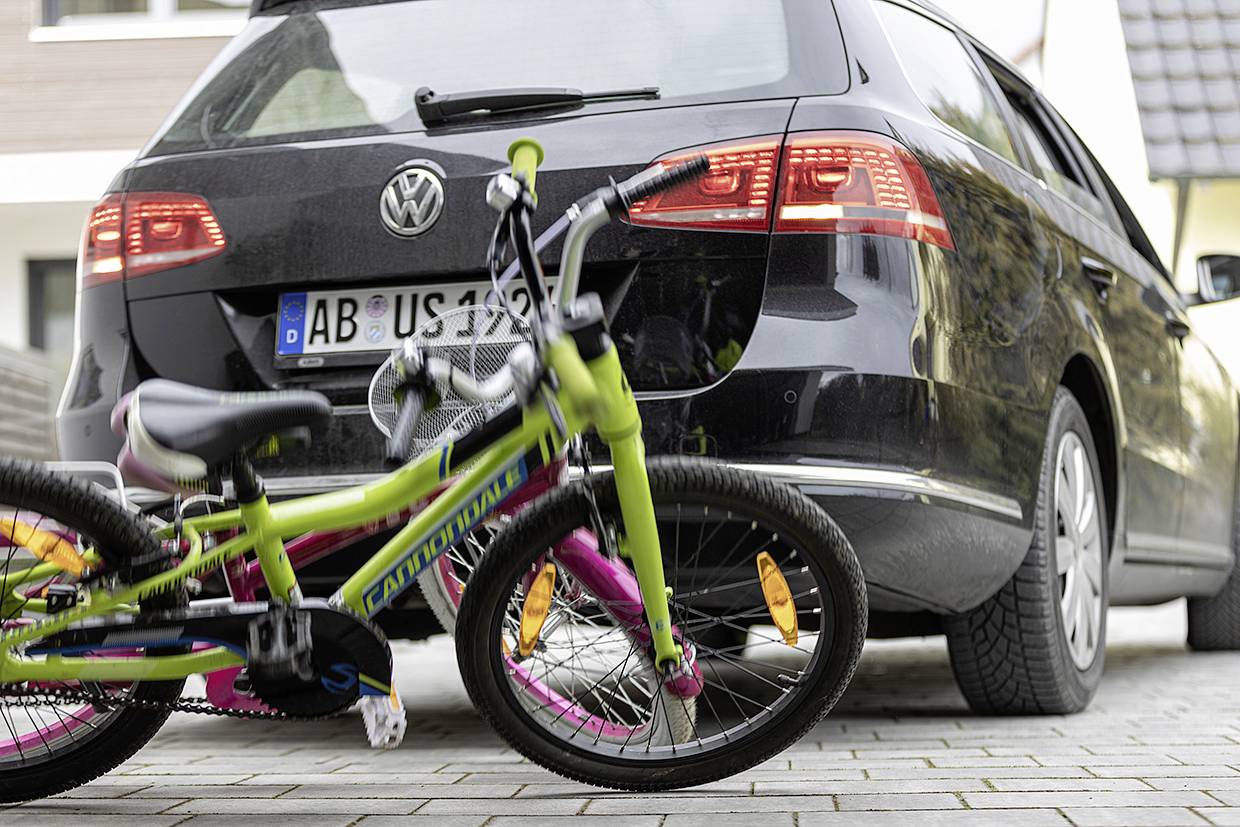 A bicycle is lying on the pavement behind a parked car. The bicycle is colourful and the car is black.