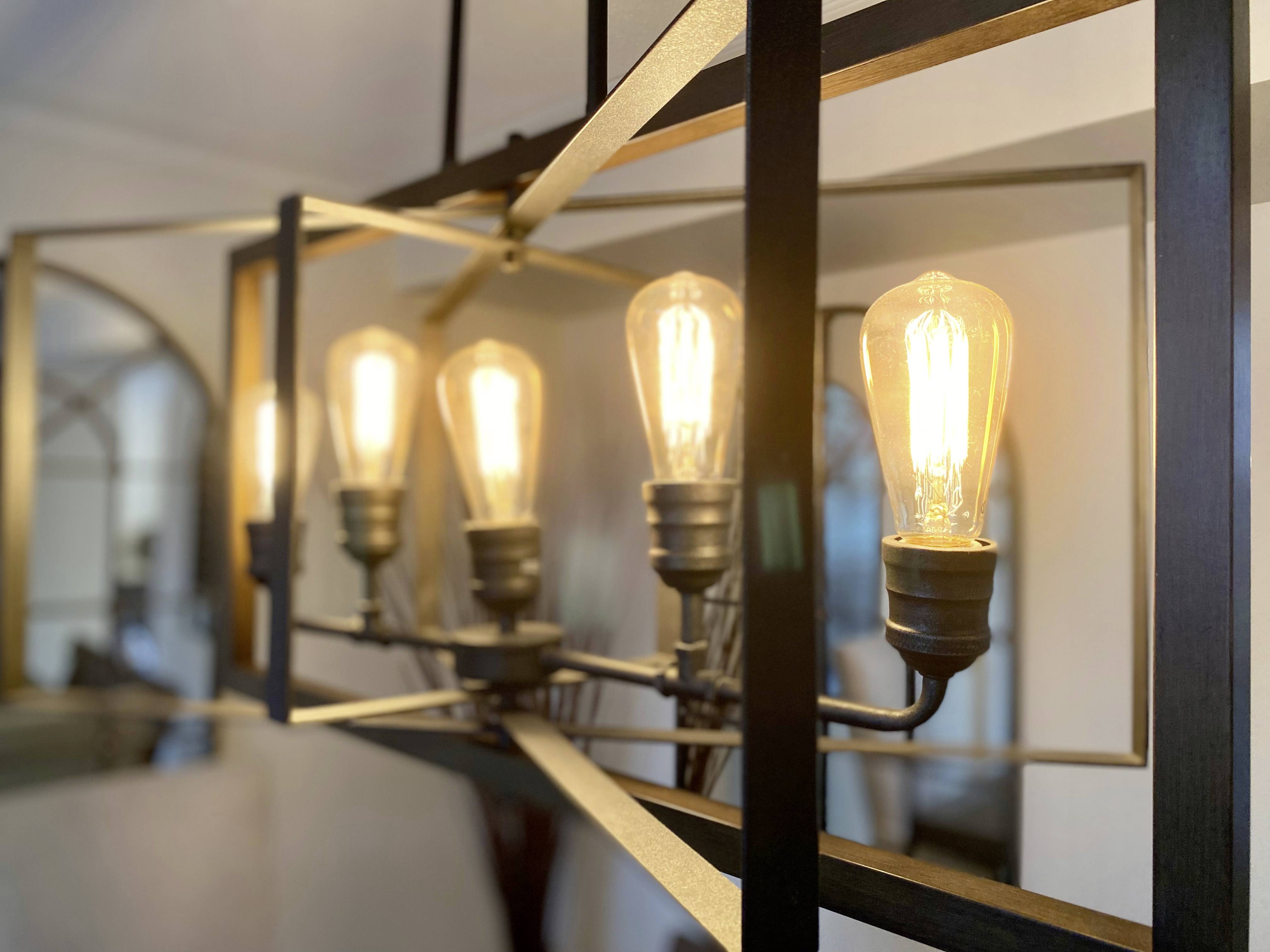 A modern chandelier with five glowing lightbulbs in a geometric metal frame, hanging in a living room.