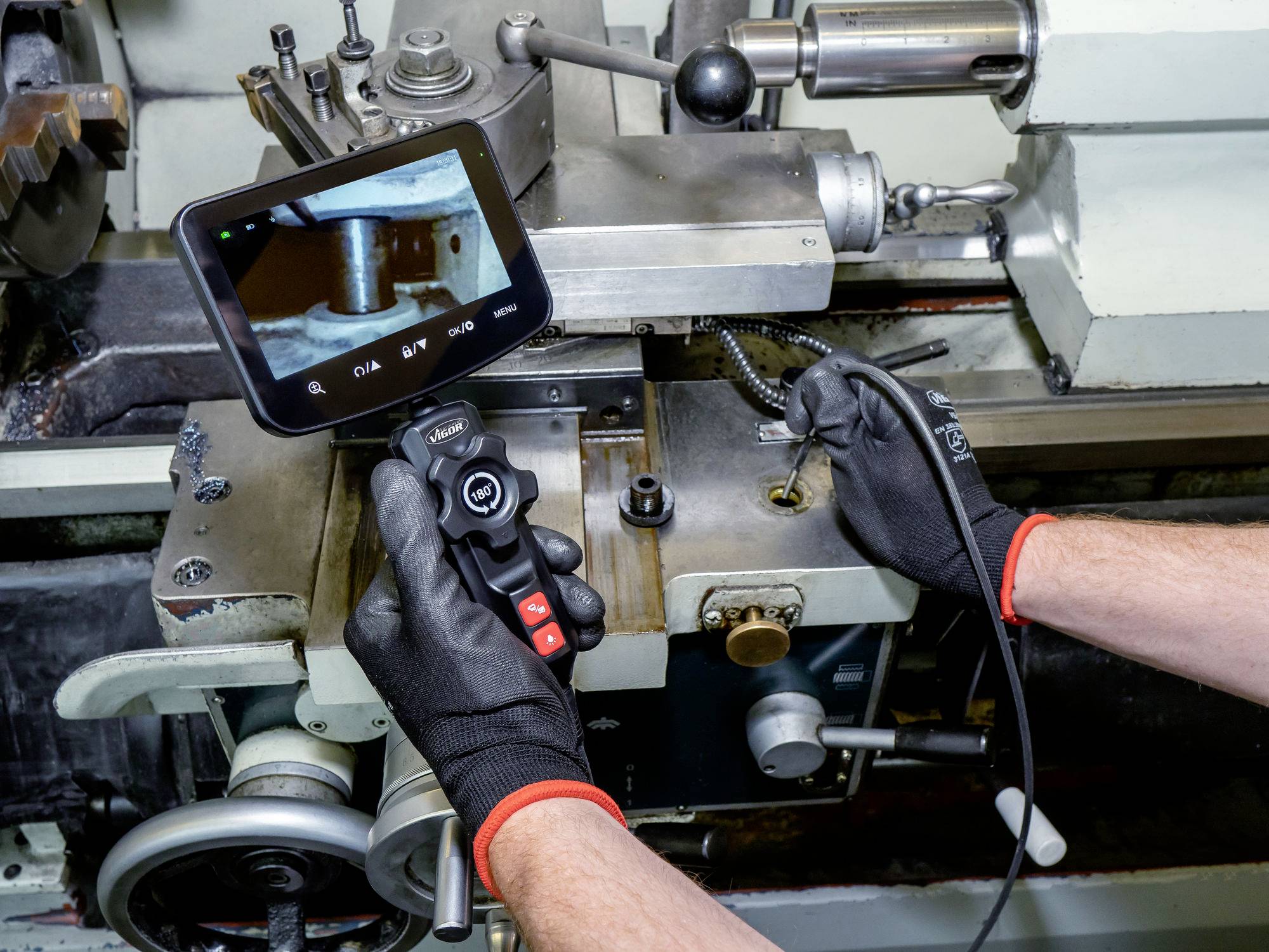 A person wearing gloves uses a borescope to inspect machinery, focusing on the screen showing the interior part of the equipment.