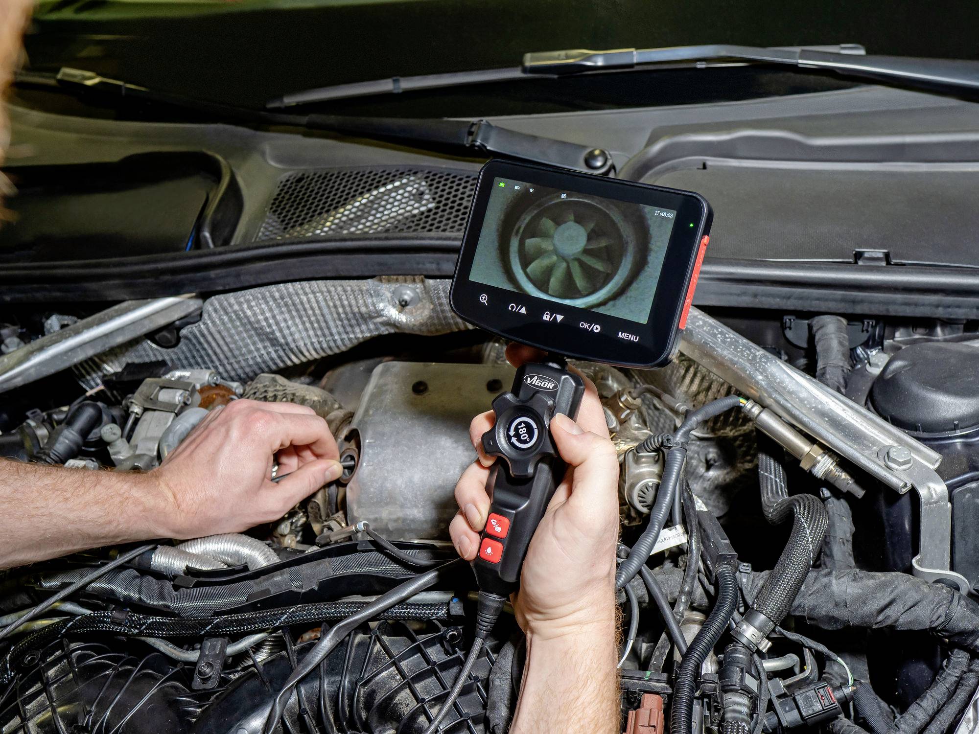 A person uses a camera device to inspect an engine. The screen shows a close-up of the engine's interior, aiding in diagnostics.
