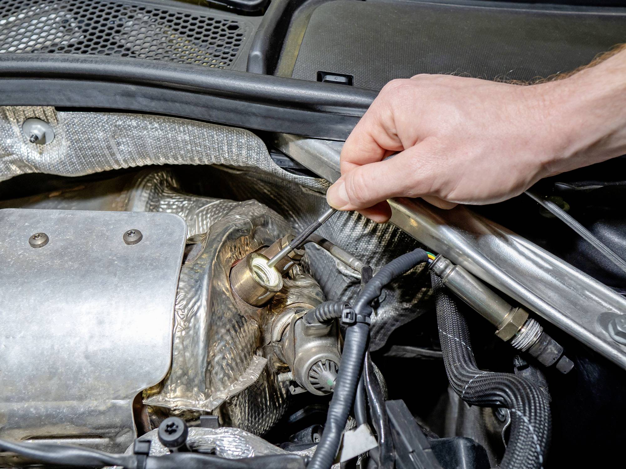 A person uses a wrench to tighten a bolt under a car hood, focusing on engine maintenance areas.