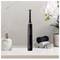 An electric toothbrush sits on a bathroom shelf next to an orchid, two rolled-up towels and a soap dispenser.