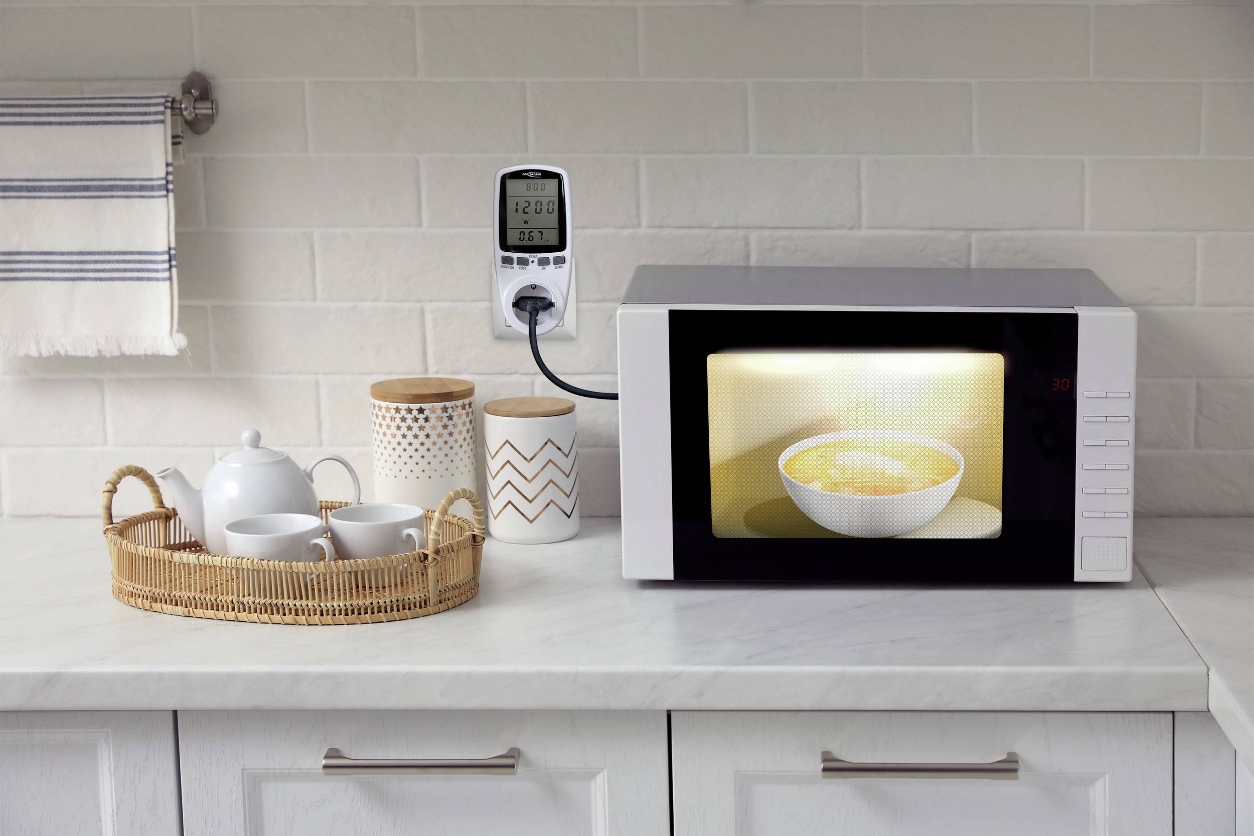 A microwave on a kitchen worktop is heating a soup bowl. Beside it are a tea set and storage containers.
