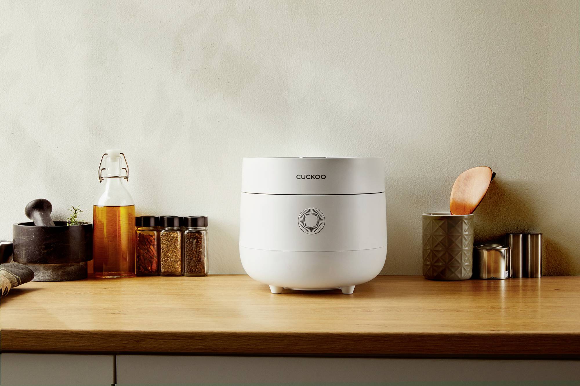 Rice cooker on a wooden kitchen worktop, surrounded by spice bottles.