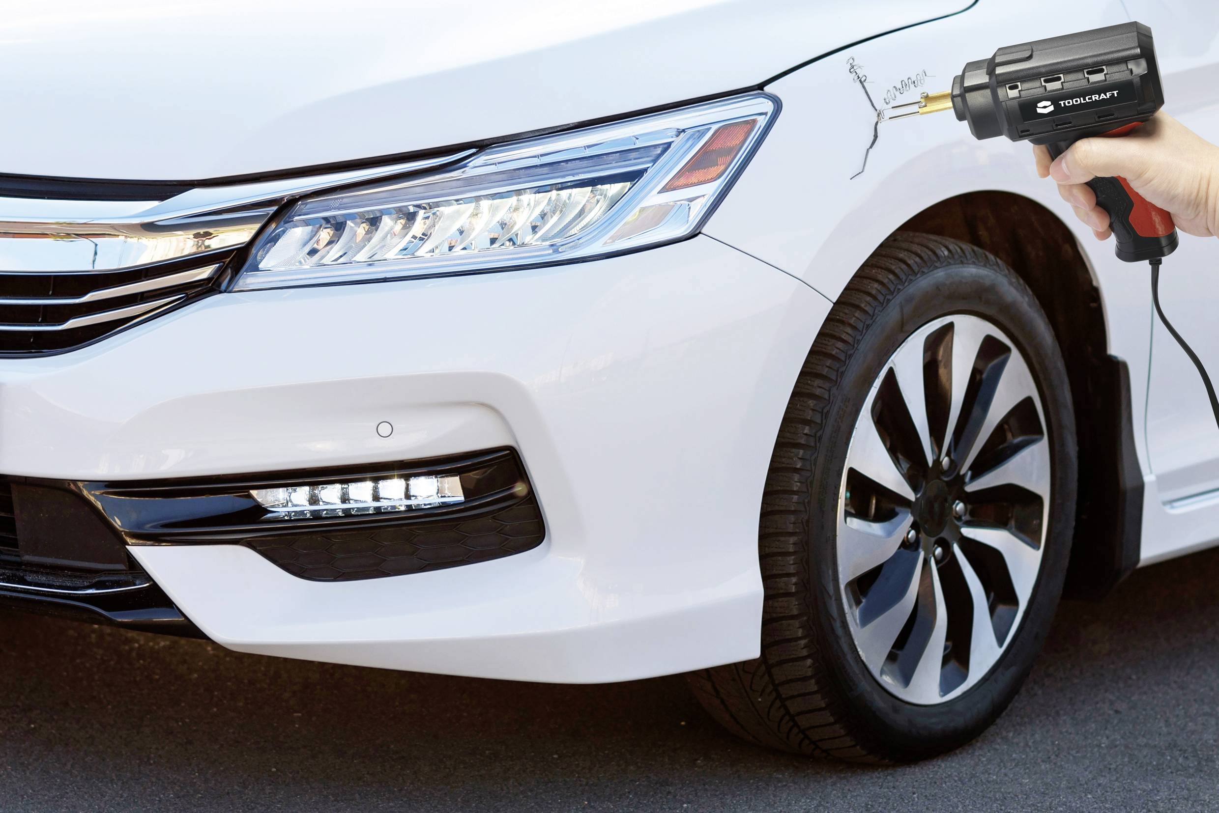 A car door has a scratch which is being treated with a portable polishing device. The vehicle is white.