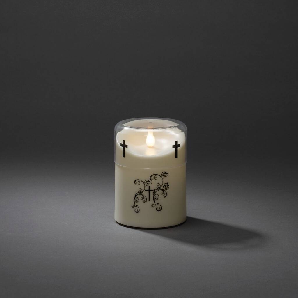 A white candle with black cross motifs, illuminating a dark room. It casts a gentle shadow to the right.