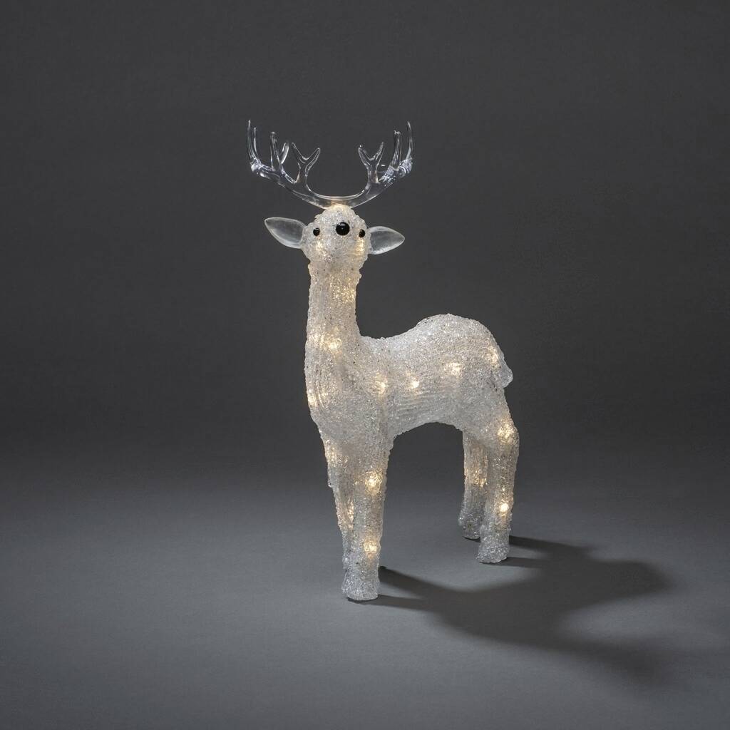 A illuminated, decorative reindeer made of crystal imitation stands against a dark background. It radiates warm light from its body.