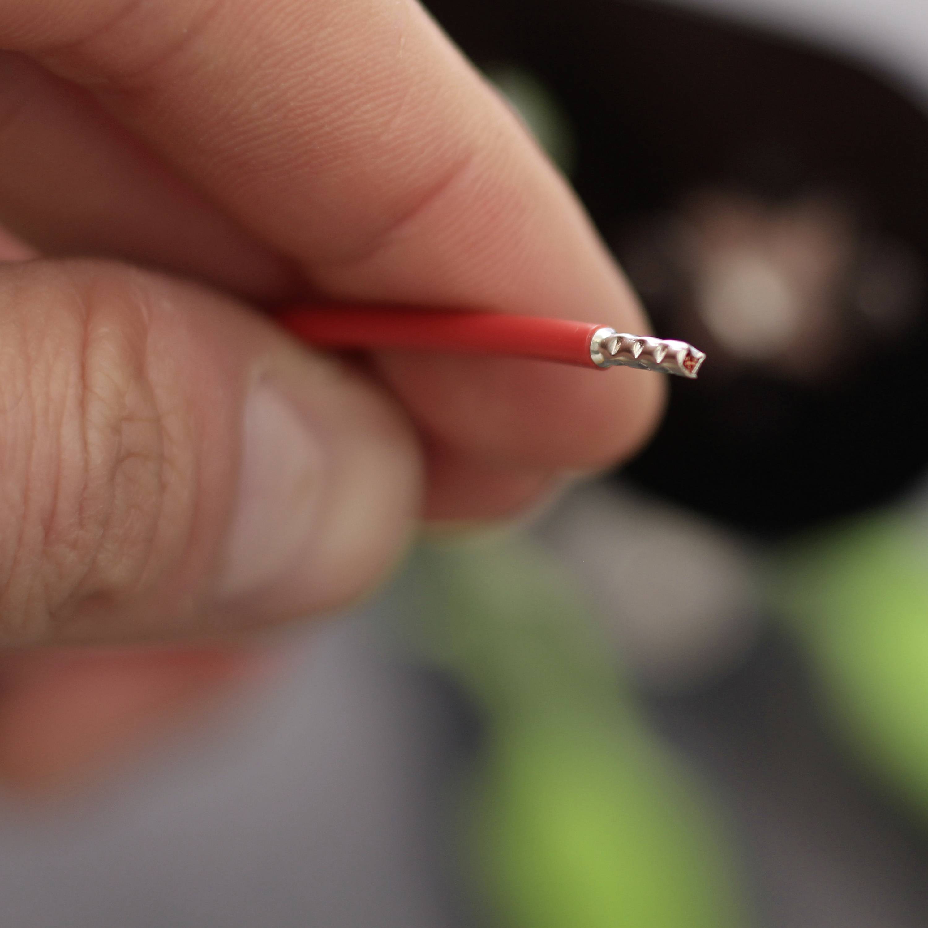 Close-up of a hand holding a red stripped cable, revealing the silver wires inside. Background blurred.