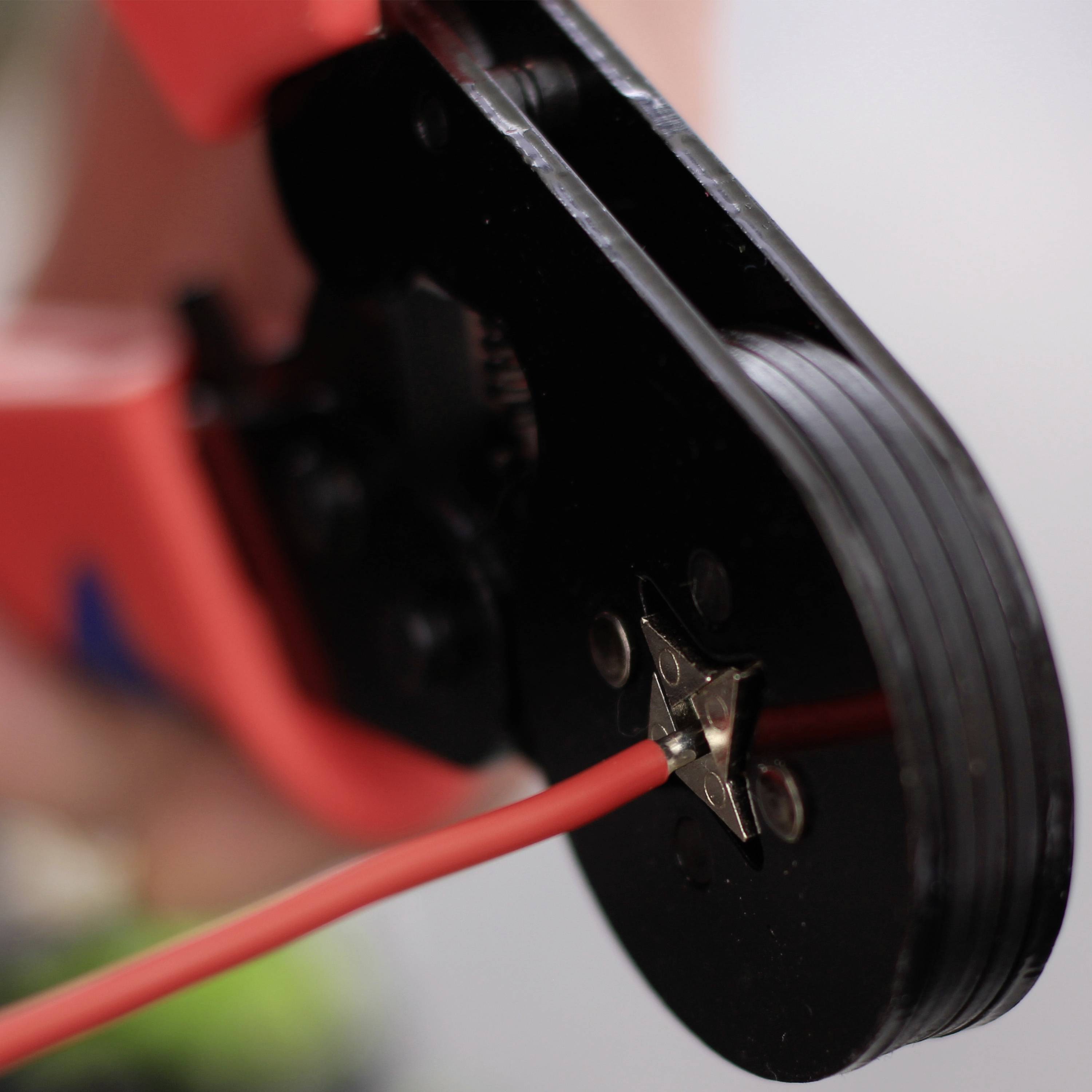 Close-up of a red crimping pliers working on a wire. Focus on the tool and the wire.