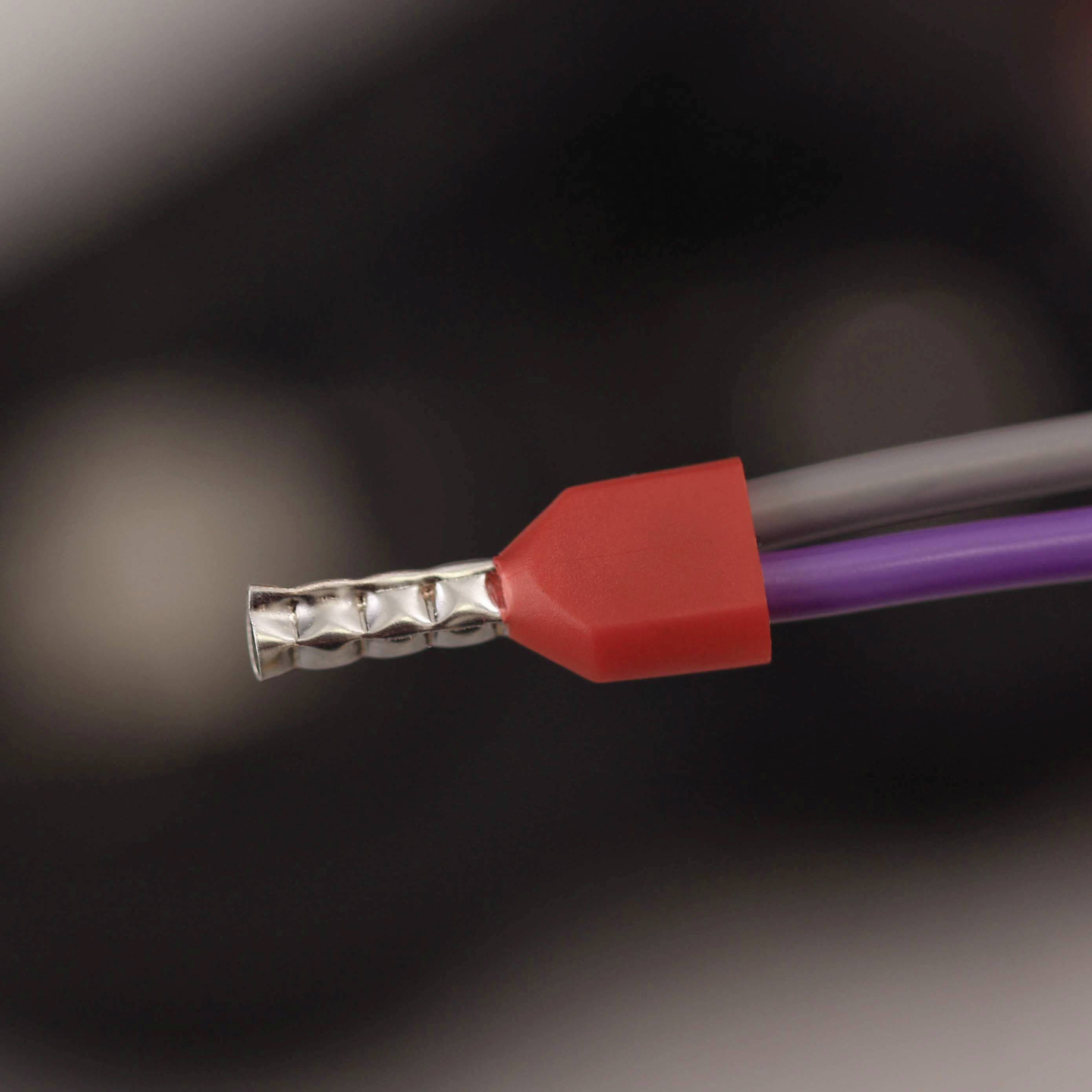 Close-up of a cable end with a metallic tip and red protective sheath. Two wires, purple and grey, are visible.