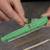 A person is holding a green electronic component holder with a resistor passed through it. Further resistors are lying in the background.
