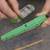 Two hands are holding a green memory module with a blue resistor on top. In the blurred background, another electrical component can be seen.