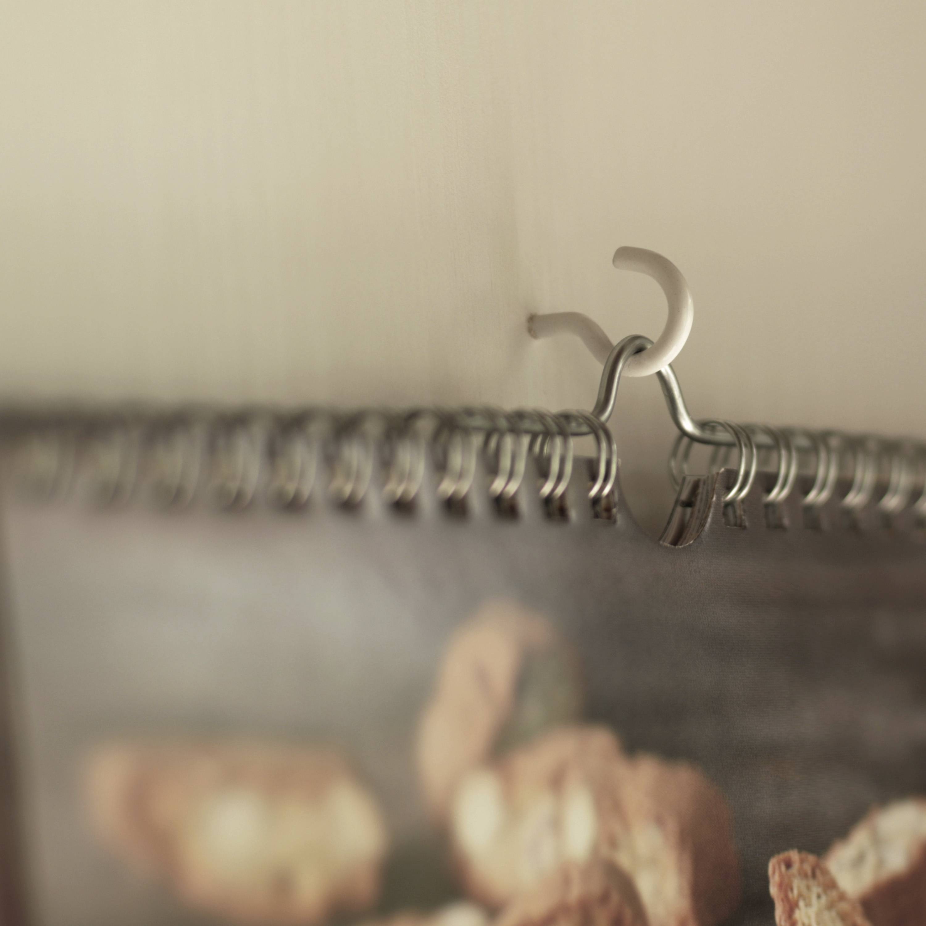 Close-up of a clip hanging a spiral-bound brochure on the wall. Details of the brochure are out of focus.