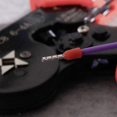 Close-up of a wire stripper gripping a red-violet cable, with the wire end exposed.