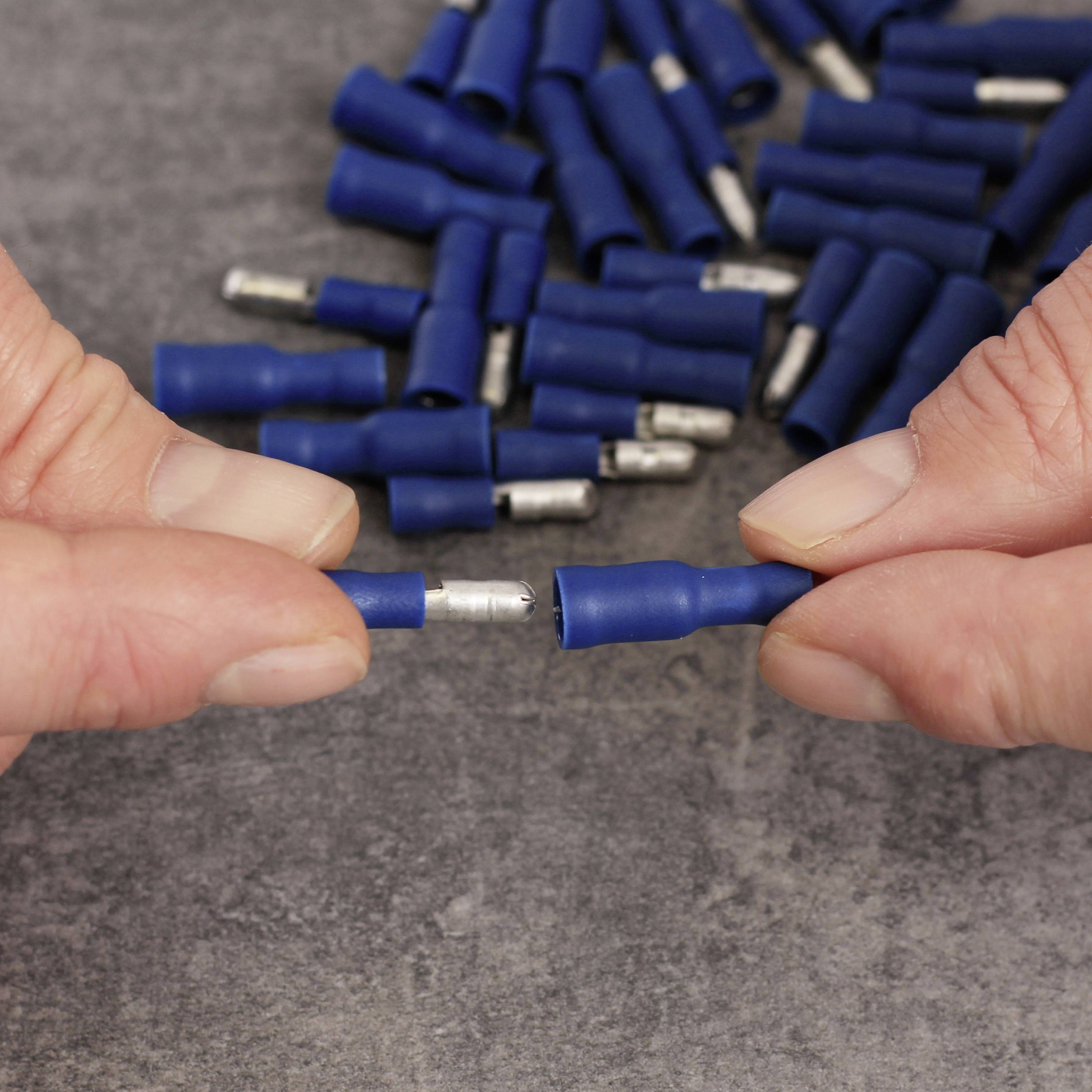 Two hands hold blue cable connectors in front of a background of additional plugs on a grey surface.