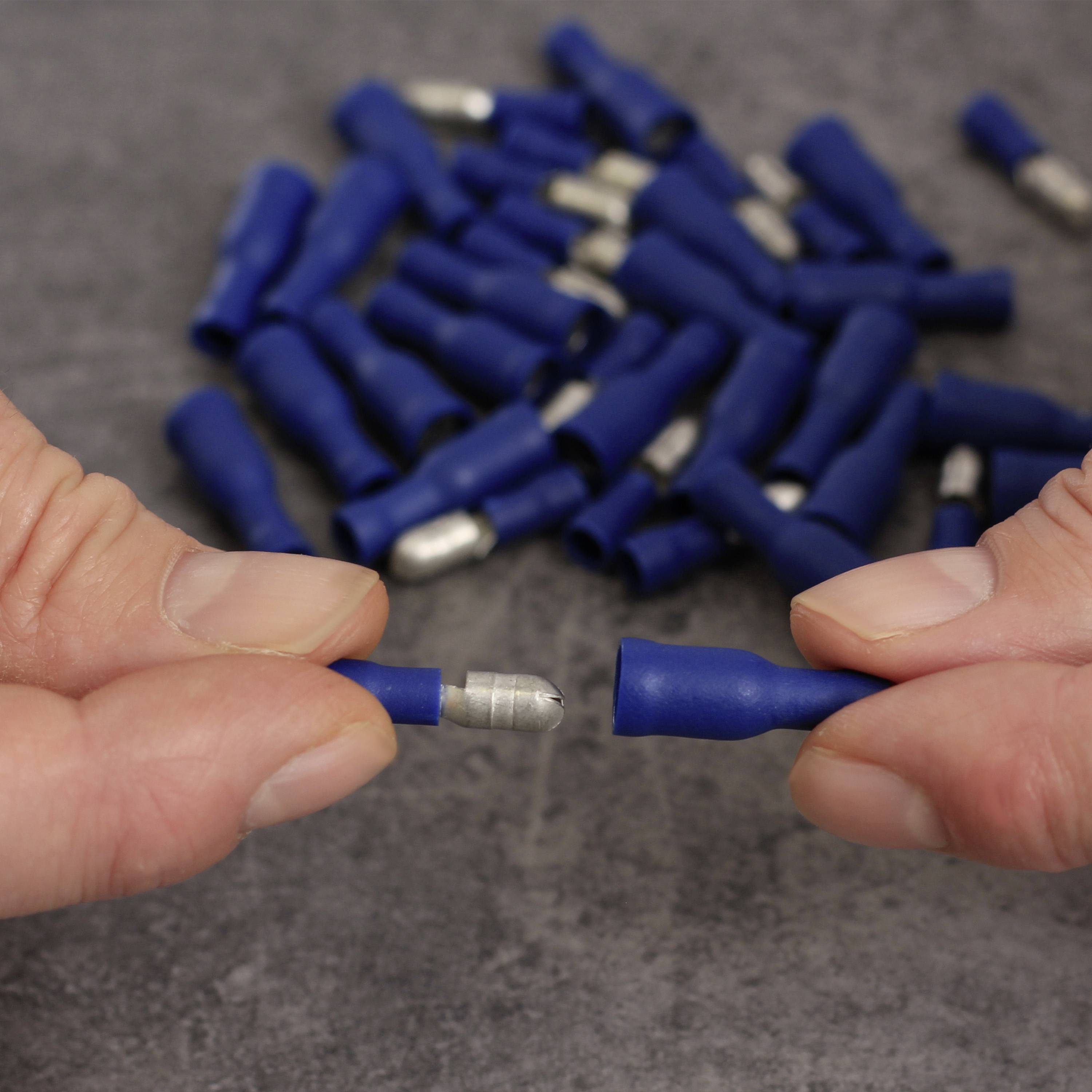 Two hands are holding a blue, insulated cable connector with a metal tip, with many other connectors lying in the background.