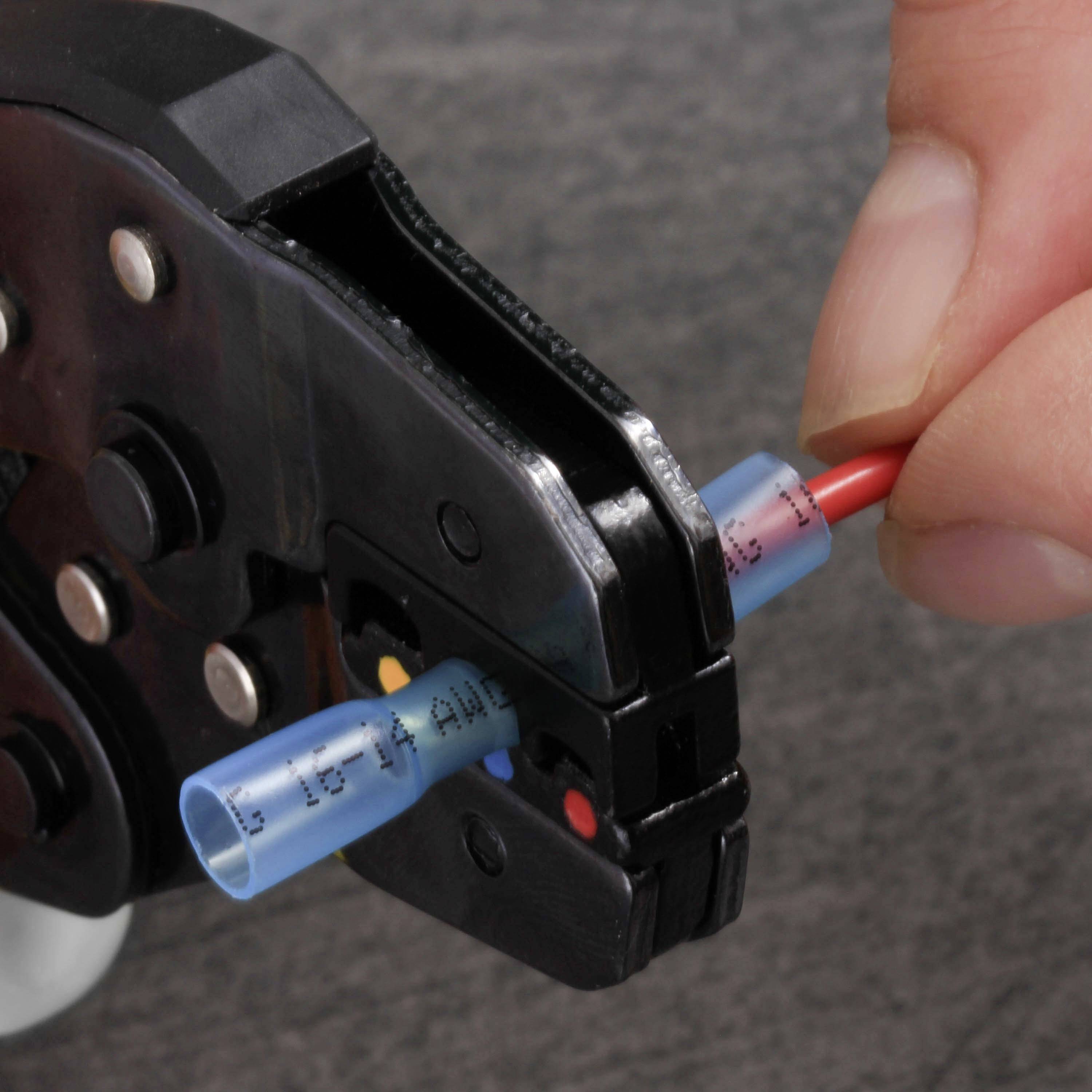 A hand is using a crimping tool to connect a red wire with a blue insulated connector.