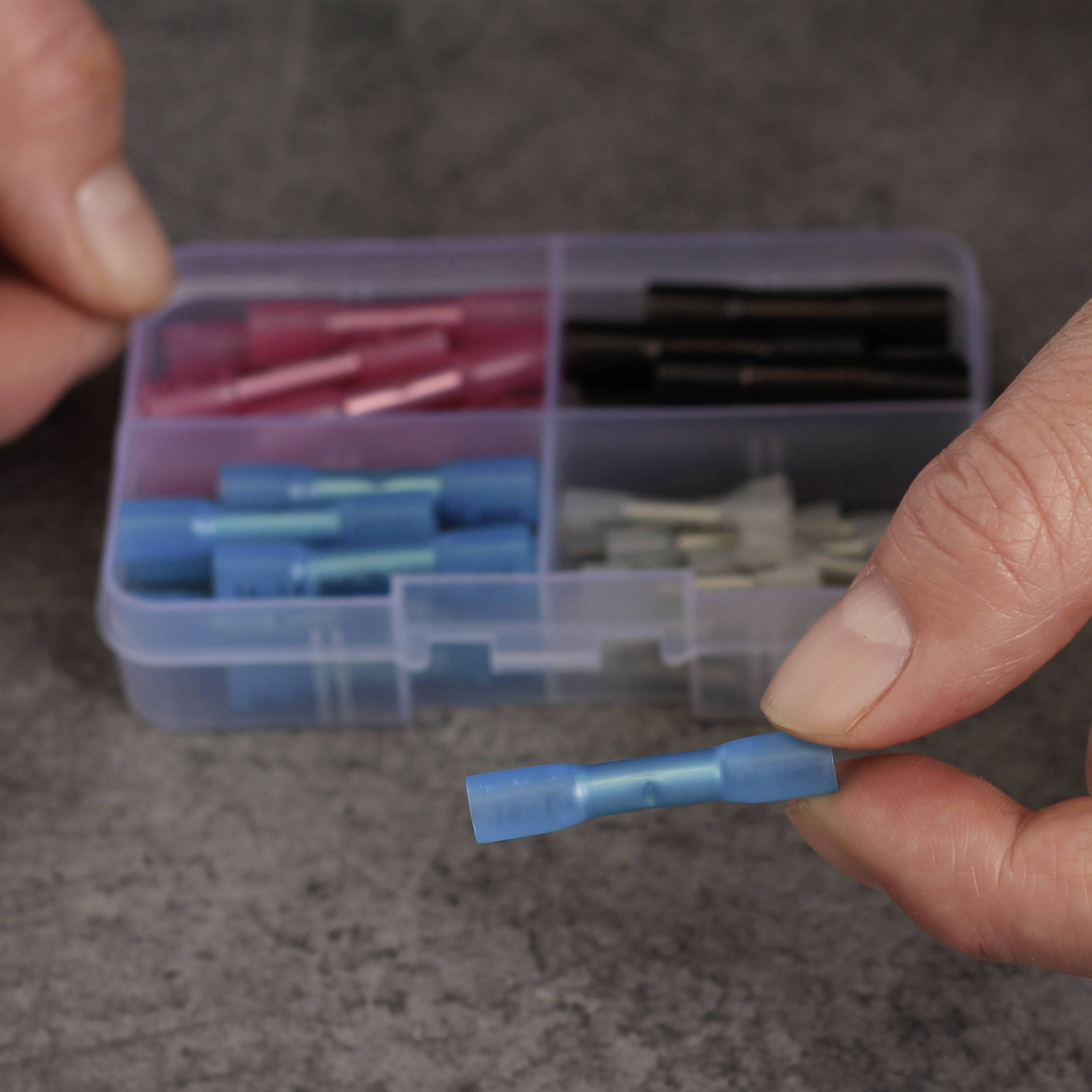 A person is holding a blue cable connector in their hand. In the background, an open box with various coloured connectors can be seen.