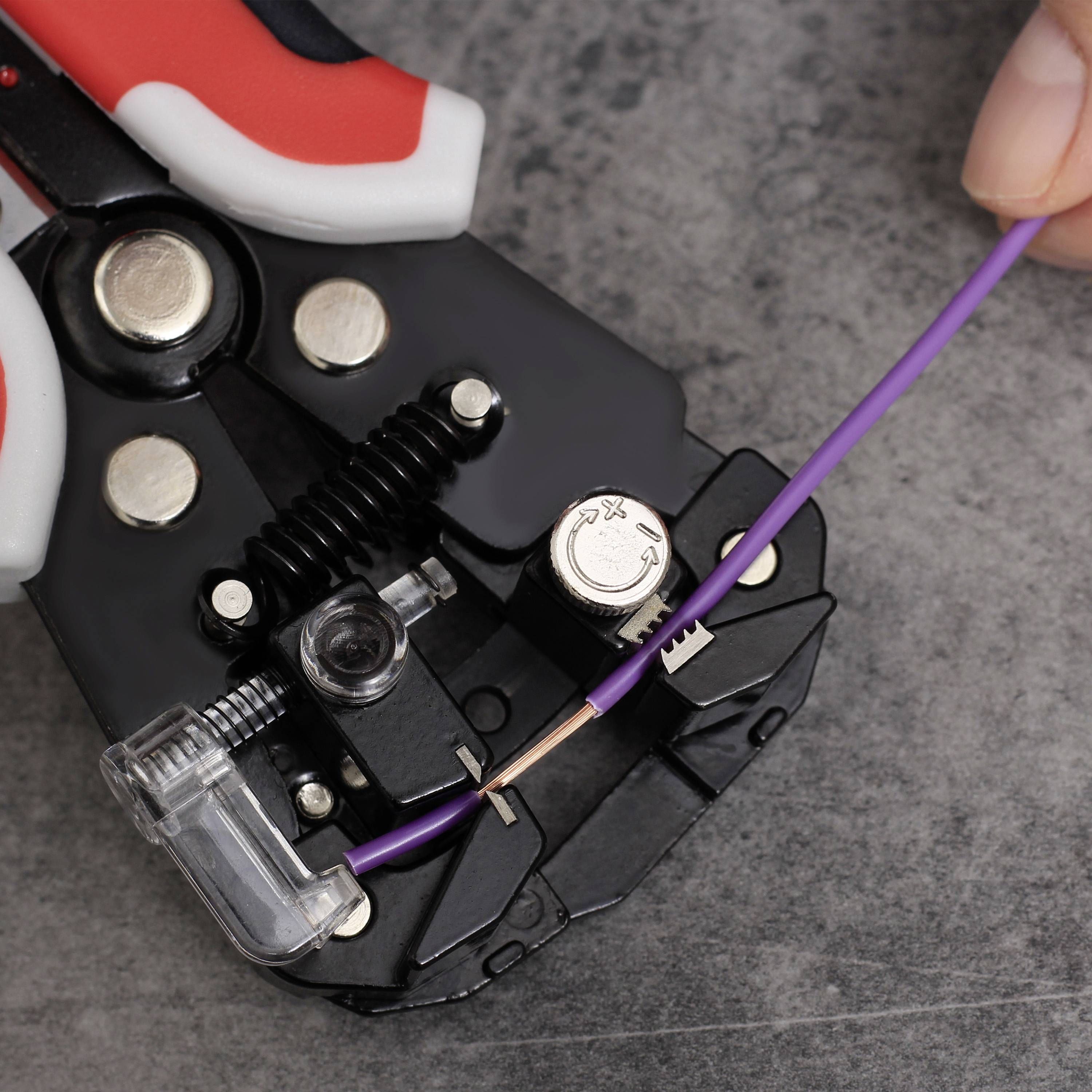 A pair of pliers removes the insulation from a purple cable. A hand holds the cable steady.