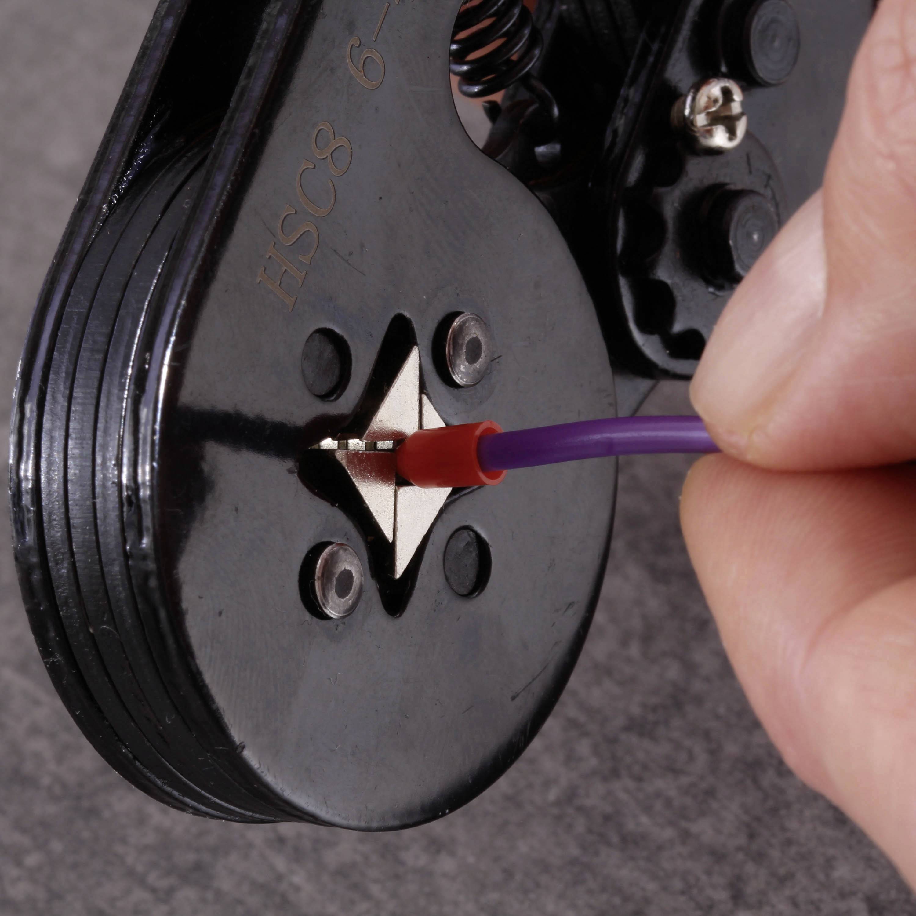 A hand is using a crimping tool to secure a purple wire in a metal connector.