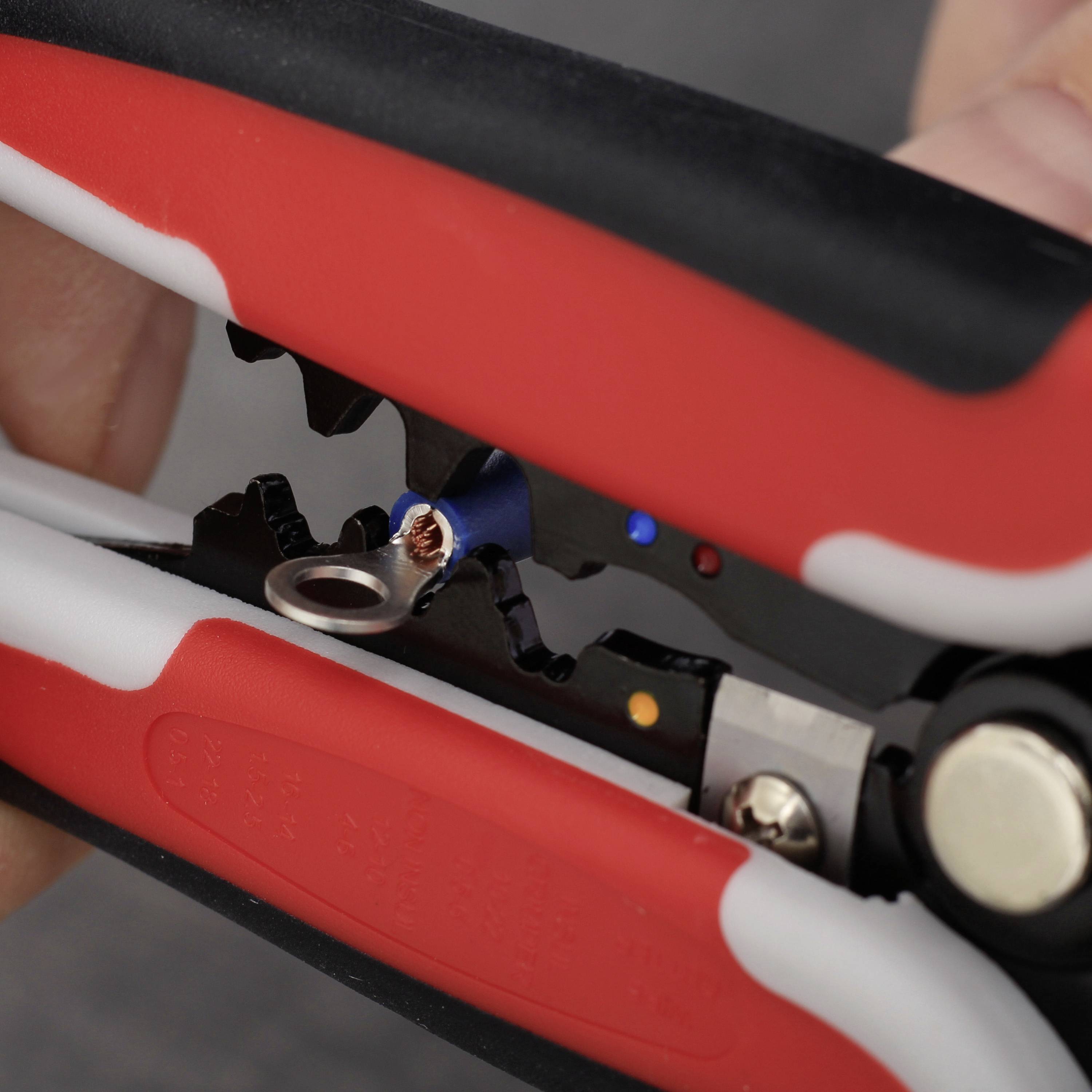 Close-up of a red wire stripping pliers stripping a cable. A metal ring is visible at the end of the wire.