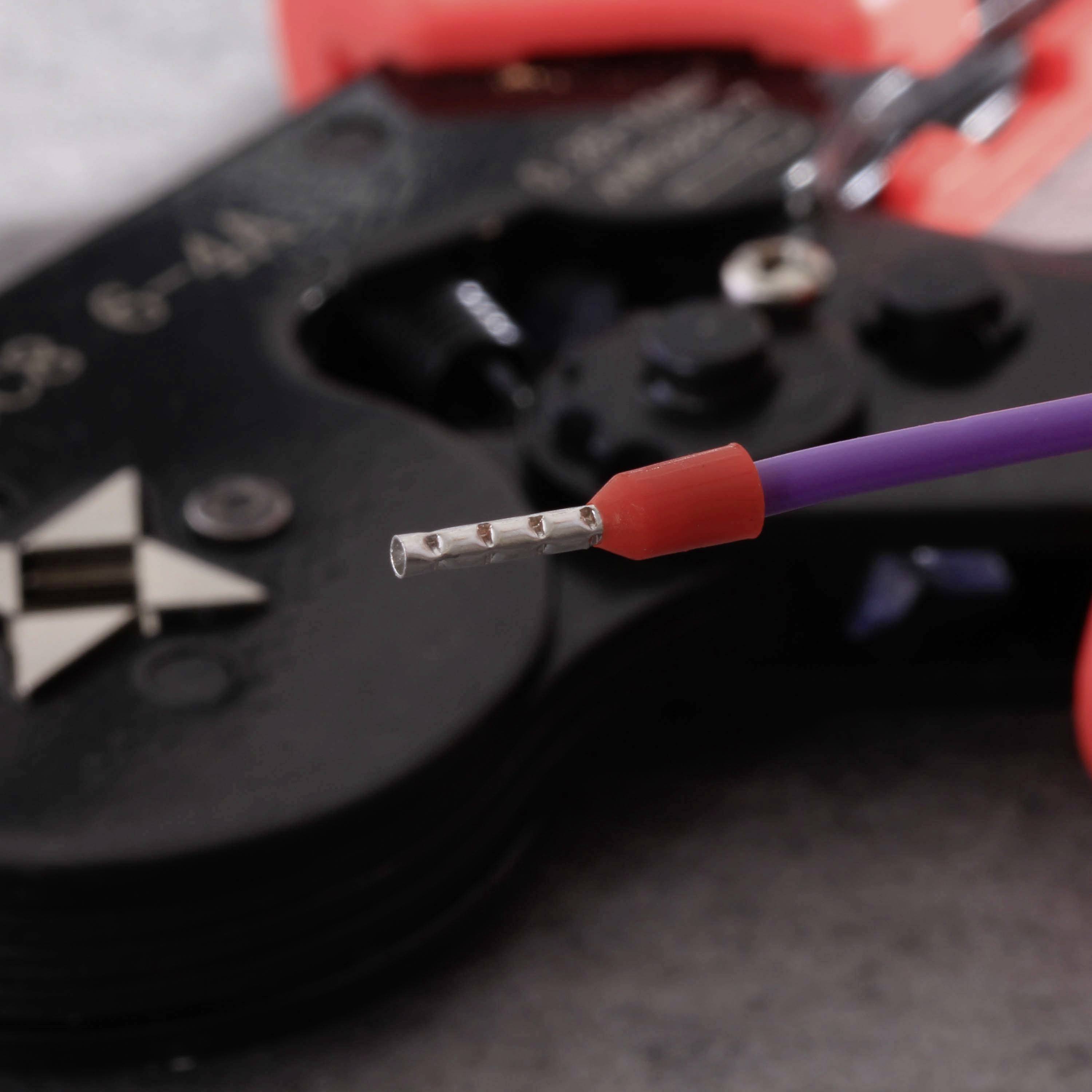 A ferrule is placed in a crimping plier, ready for processing. The crimping plier has a red and purple handle.