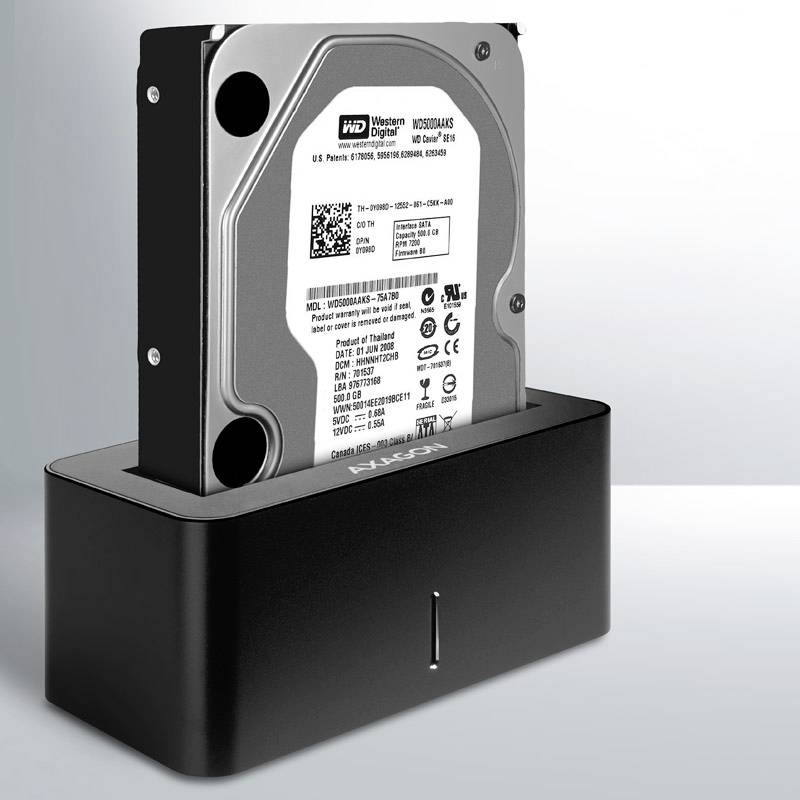 A hard drive is seated in a black docking station. The hard drive is positioned vertically, and the front side displays relevant technical information.