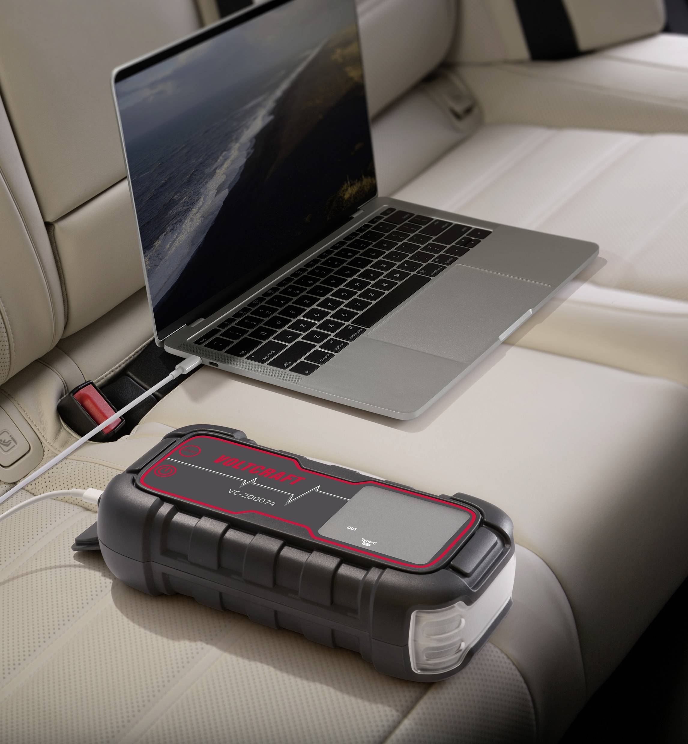 A laptop is being charged on the back seat of a car using a portable charger. The charger indicates a fully charged state.