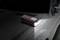 A portable battery charger illuminates on the bonnet of a vehicle covered in water droplets in a dark environment.