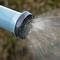 A blue garden hose sprays a jet of water into the air against a blurred background, presumably outdoors.