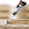 A person is using a cordless vacuum cleaner to remove dirt from a wooden floor, with a clearly visible cleaned area.